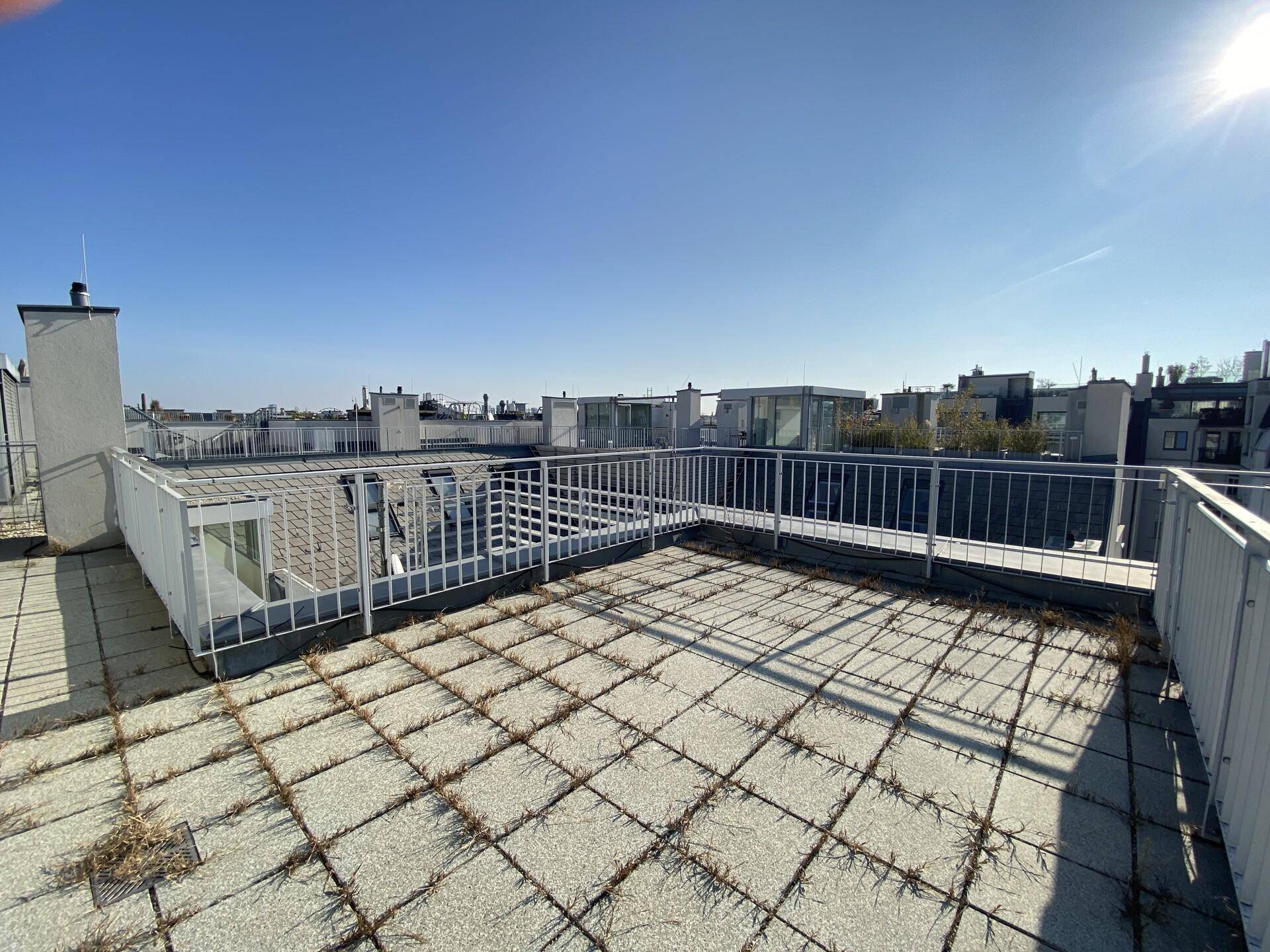 Weitläufige Dachterrasse mit Fliesenboden und Panoramablick unter blauem Himmel.