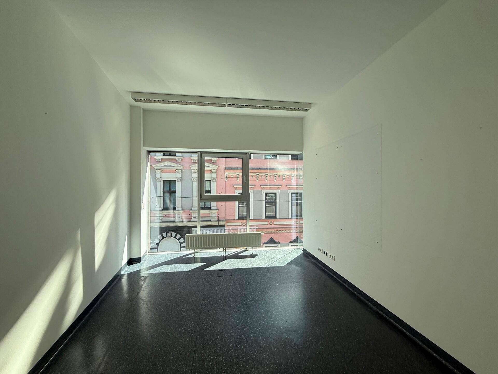 Heller Büroraum mit großem Fenster und Blick auf ein historisches Gebäude gegenüber der Straße.