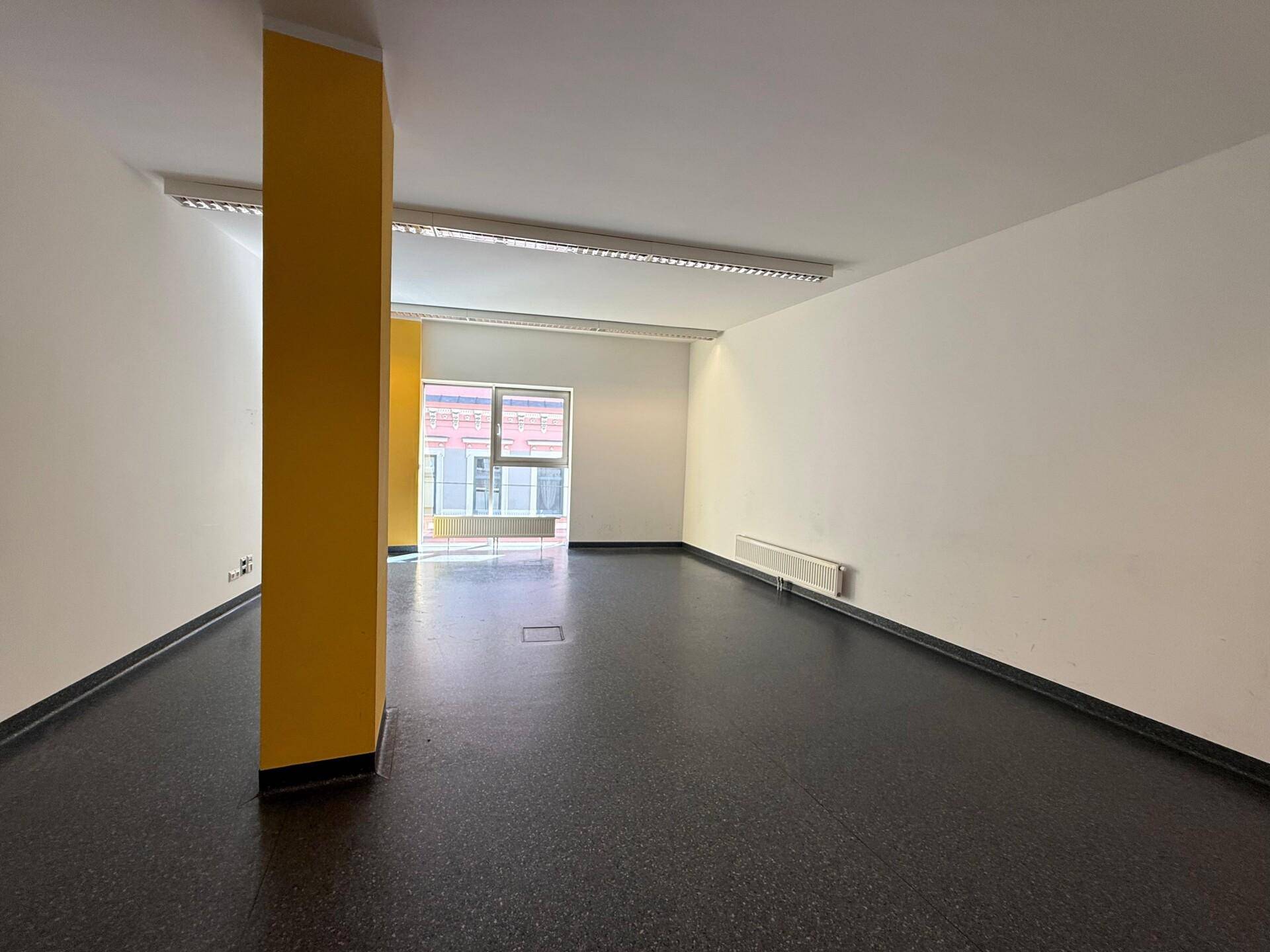 Geräumiger Büroraum mit einem auffälligen gelben Pfeiler und Fenster mit Blick auf die Stadt.