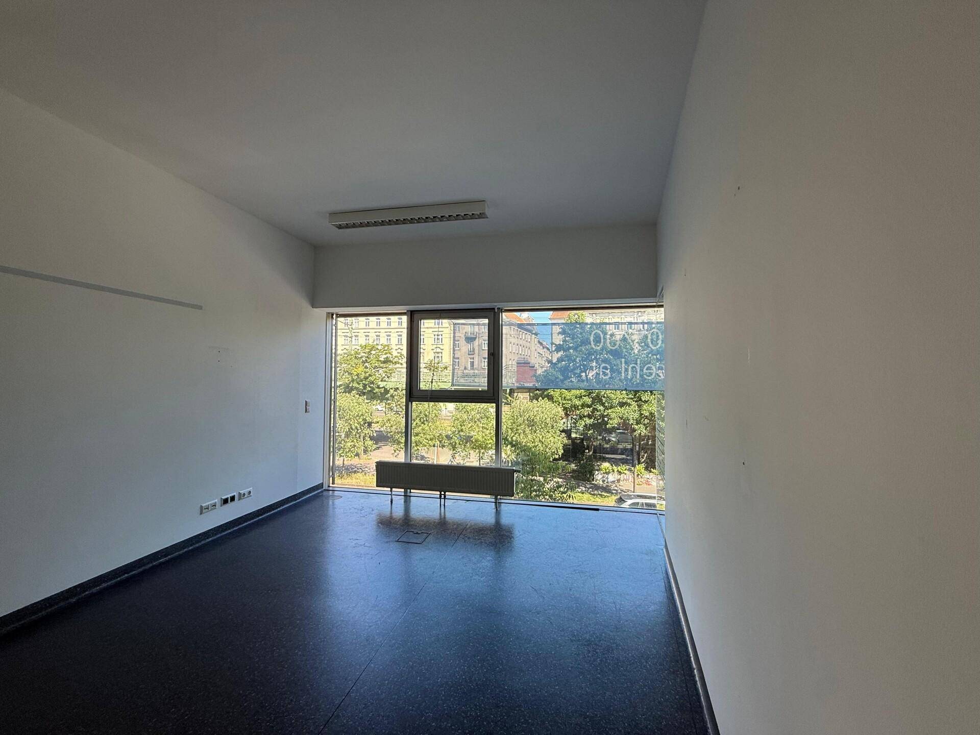 Heller Büroraum mit Fensterfront und Blick auf Bäume und die belebte Straße.