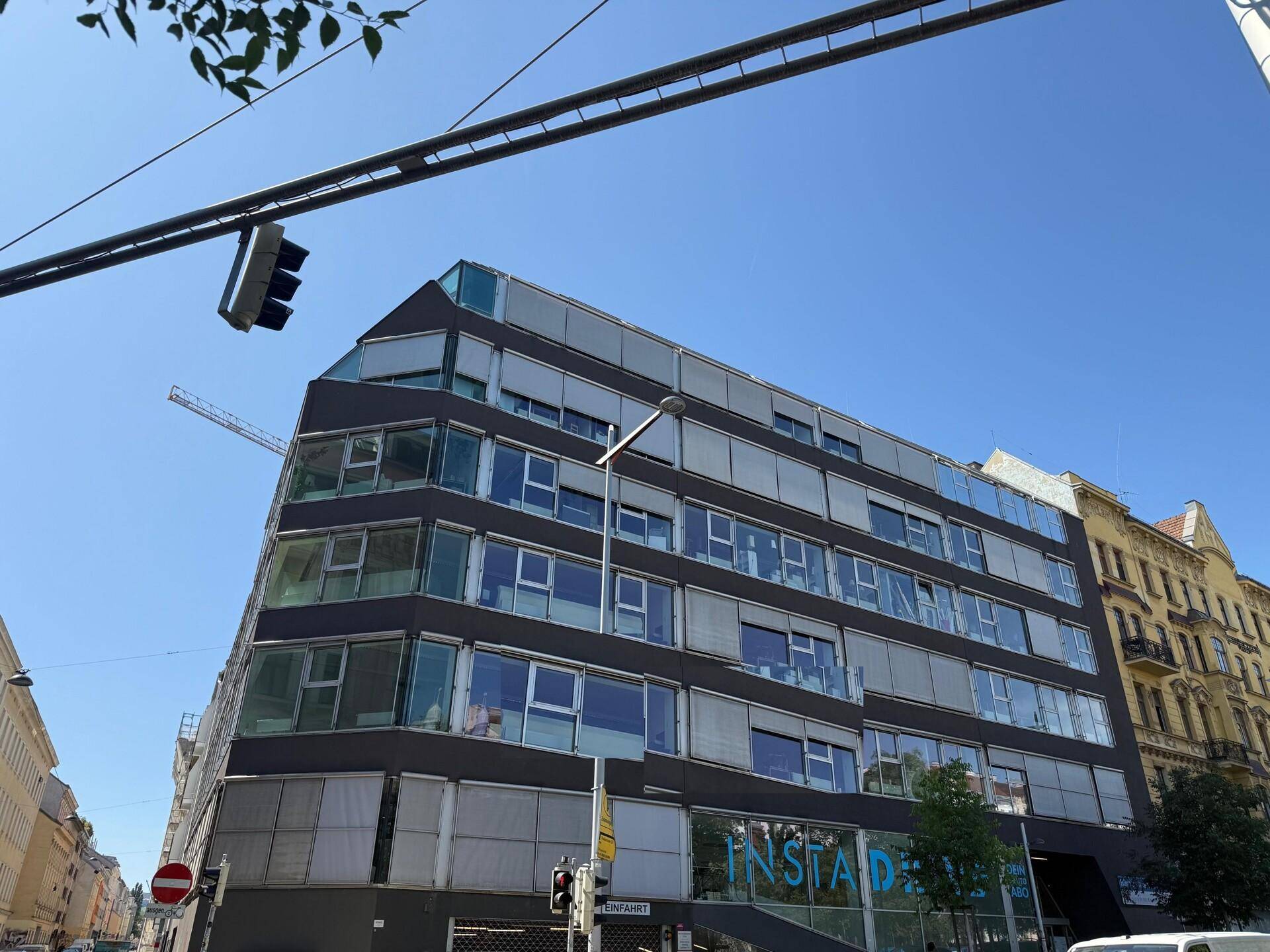 Zeitgenössisches Bürogebäude mit vielen Fenstern und Außenjalousien unter strahlend blauem Himmel.