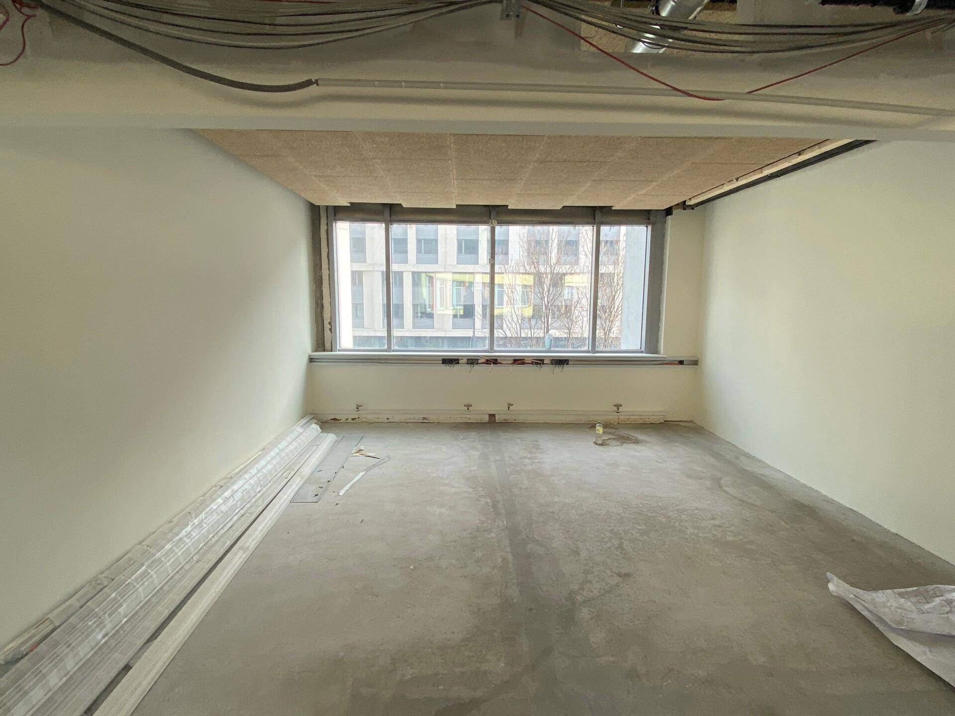 Leerer Büroraum im Rohbau mit Betonboden, weißen Wänden und einem großen Fenster.