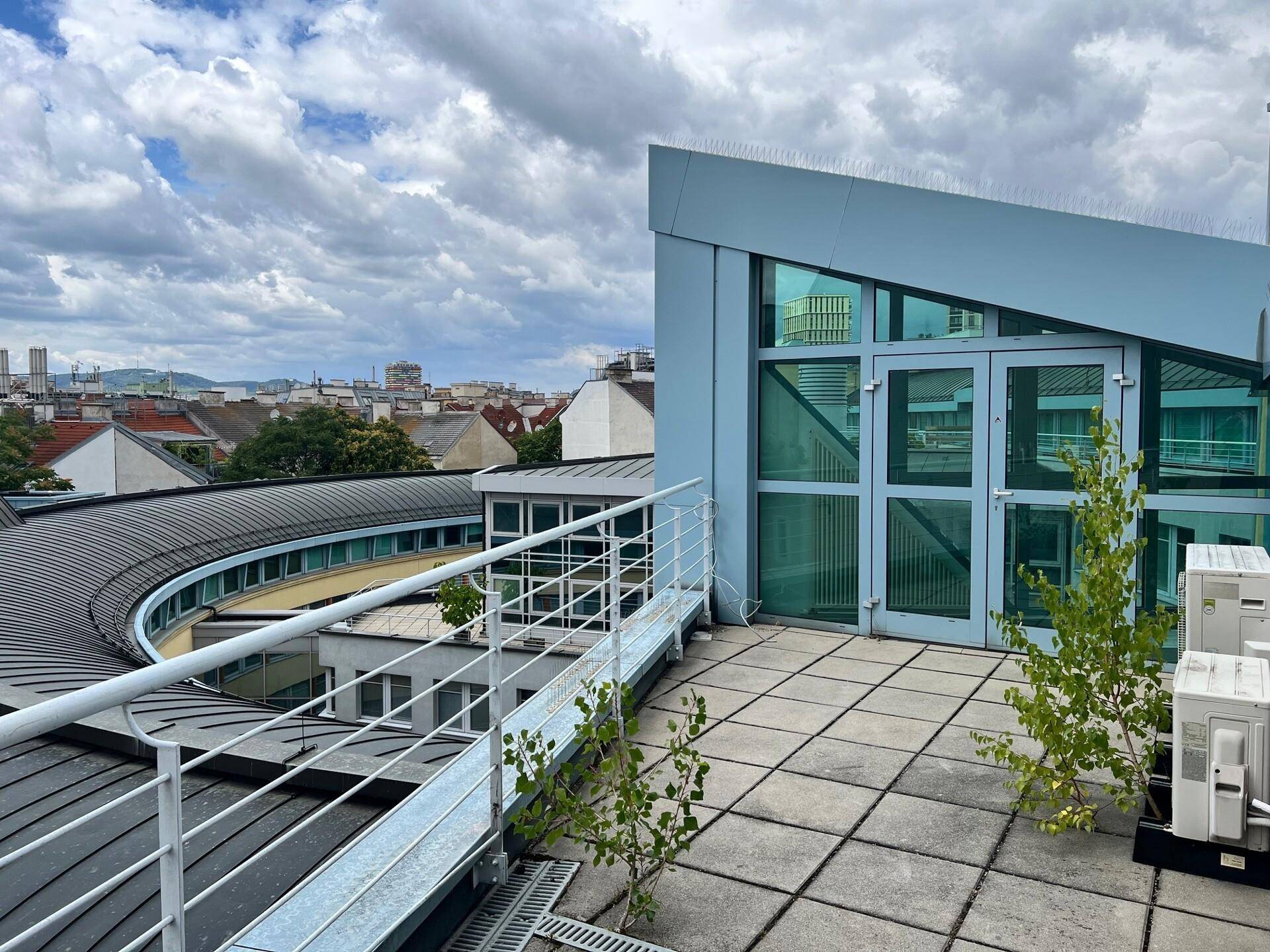 Dachterrasse mit Stadtblick, gepflastertem Boden und moderner Glasfassade des Gebäudes.