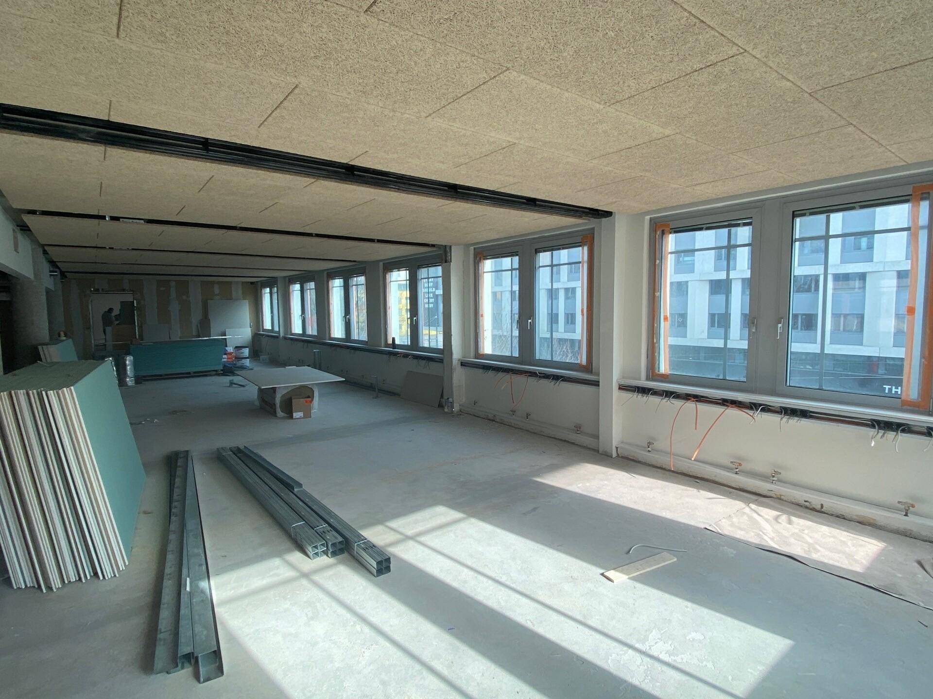 Großer, unmöblierter Bürobereich im Rohbau mit Betonboden, Akustikdecke und vielen Fenstern.