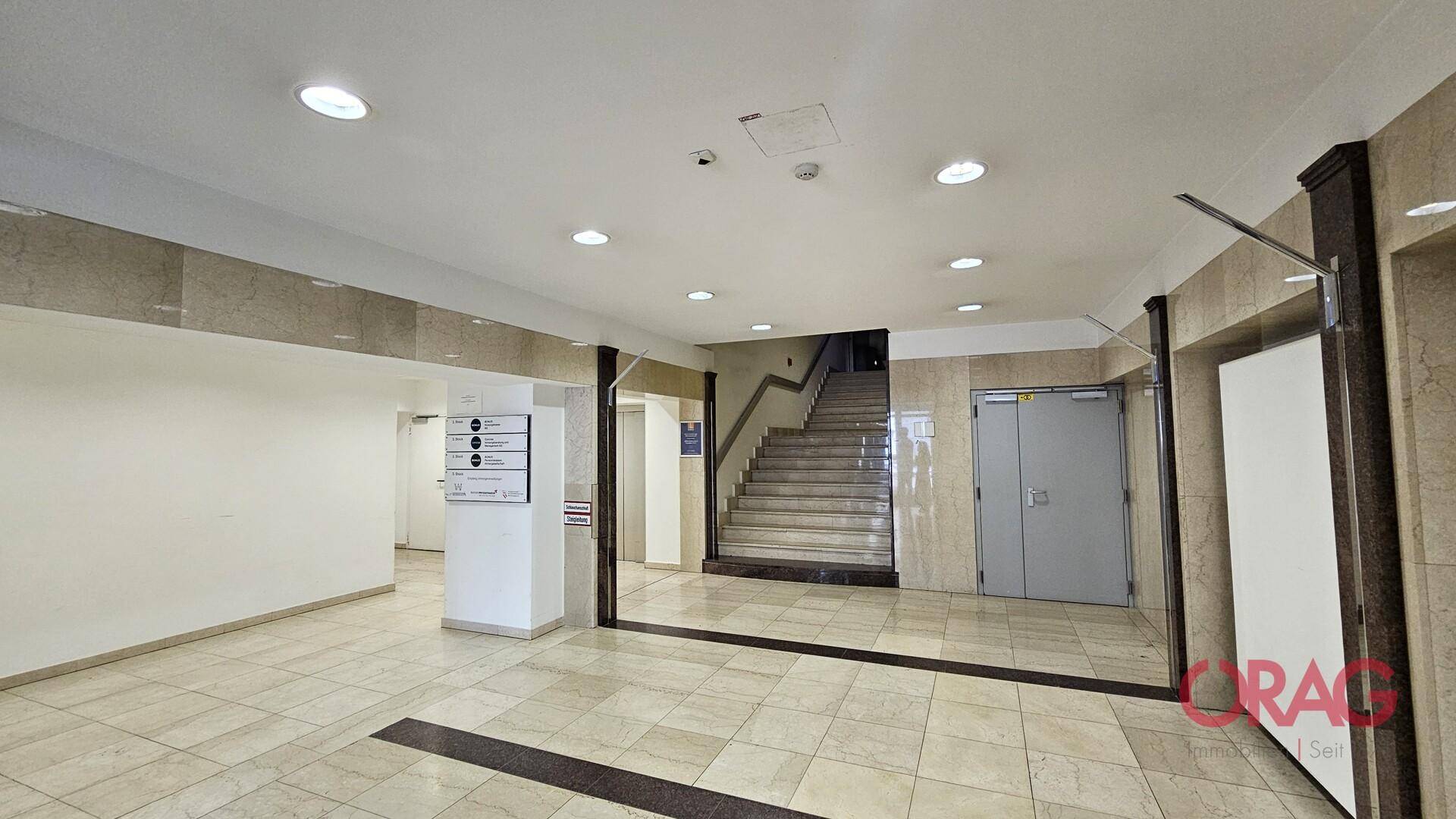 Heller Flurbereich mit eleganten Marmorfliesen und einer breiten Treppe, die in die oberen Stockwerke führt.