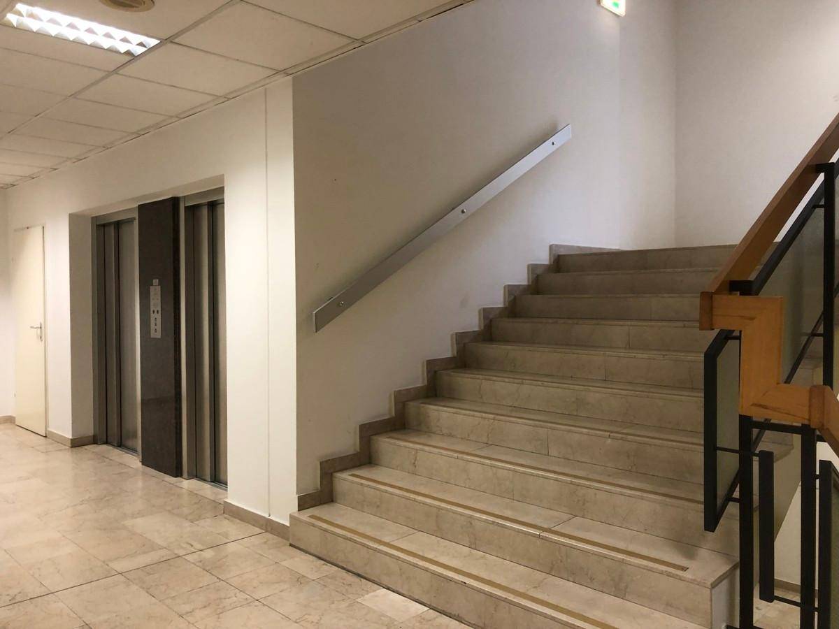 Treppenhaus mit Marmorstufen und einem modernen Geländer, neben dem sich ein Aufzug befindet.