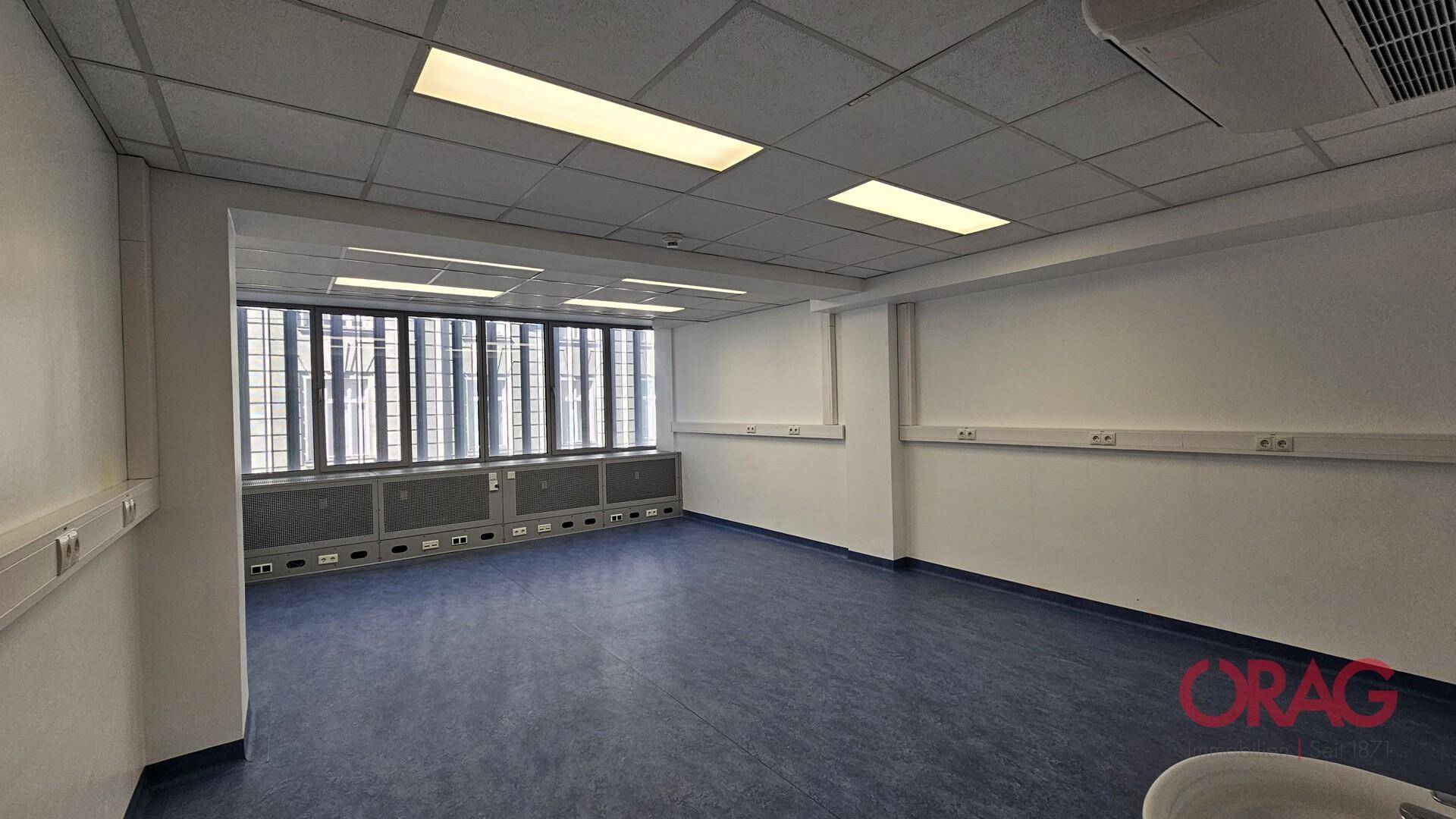 Kleineres Büro mit Fenstern, Jalousien und einer Klimaanlage, ideal für konzentriertes Arbeiten.