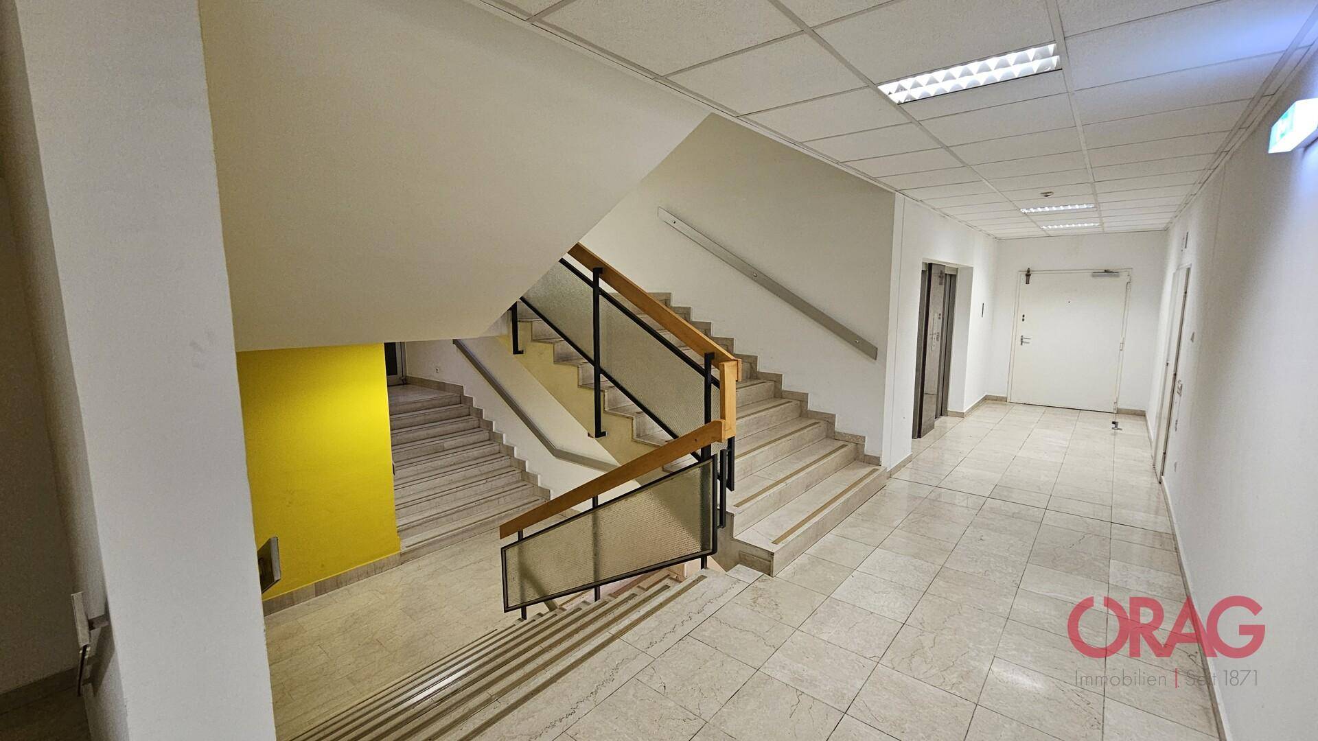 Helles Treppenhaus mit Marmorstufen, Holzgeländer und einer auffälligen gelben Akzentwand.