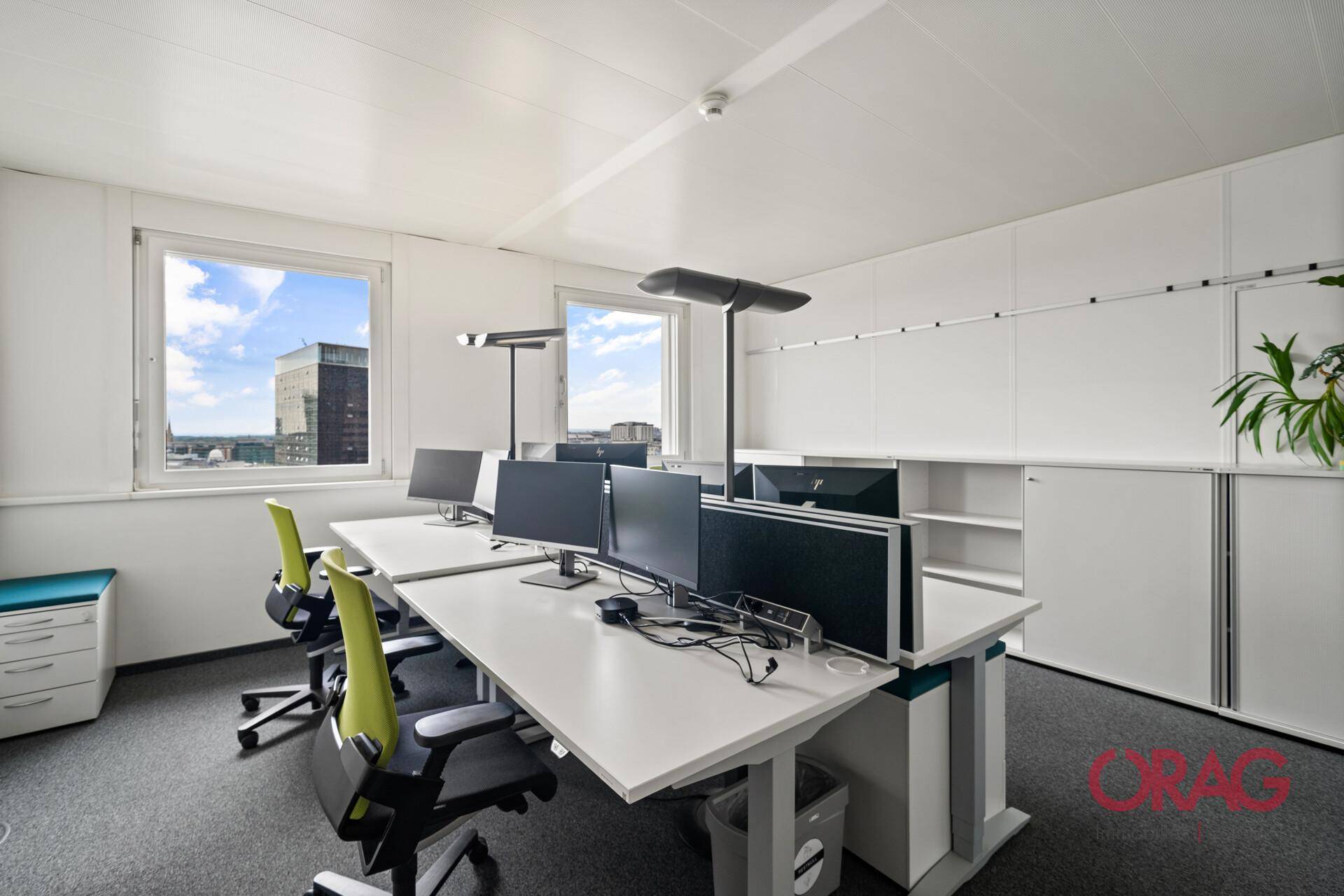 Modernes Büro mit zwei Arbeitsplätzen, weißen Schränken und Blick auf die Stadt.