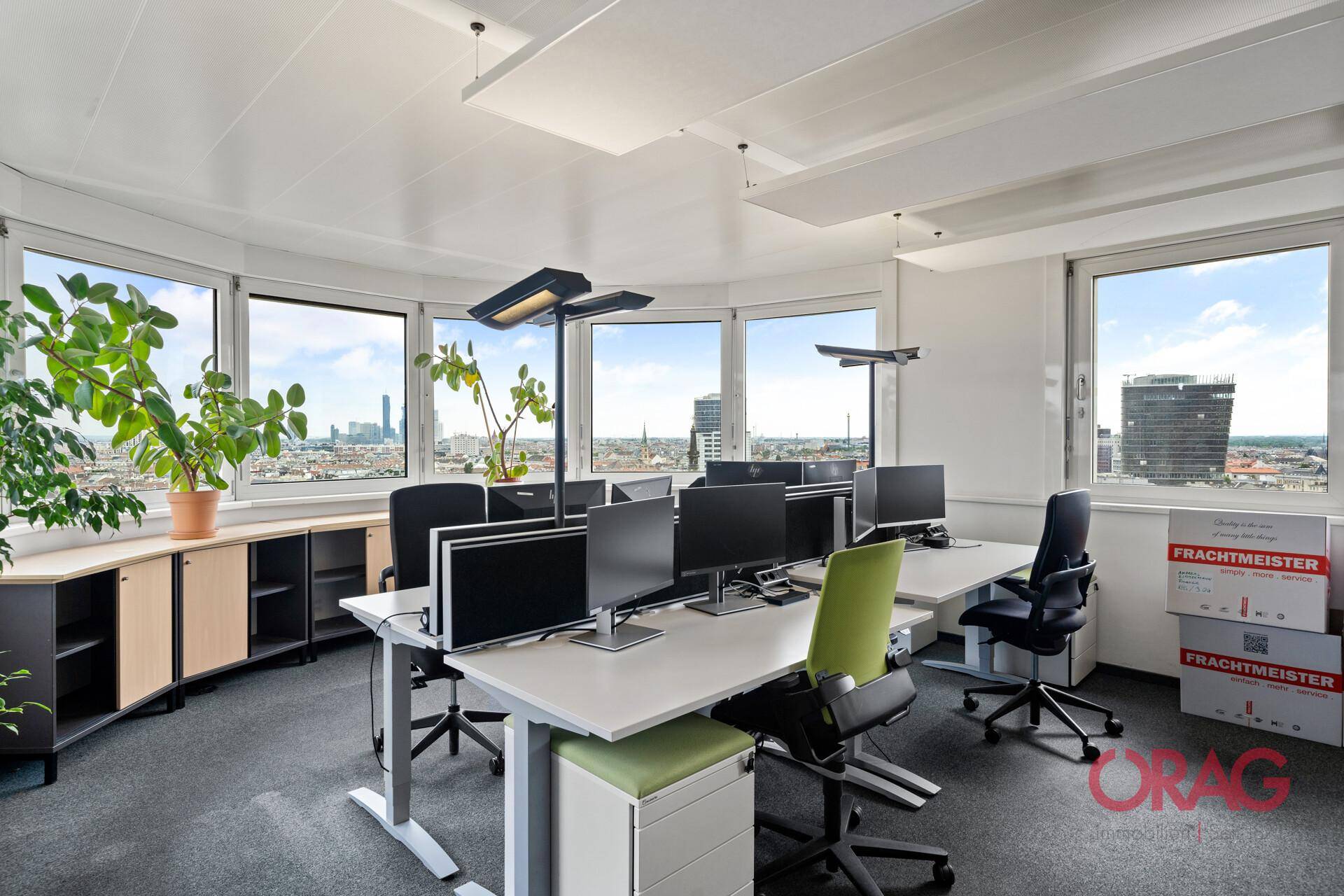 Helles Büro mit mehreren Arbeitsplätzen, großen Fenstern und Stadtblick.