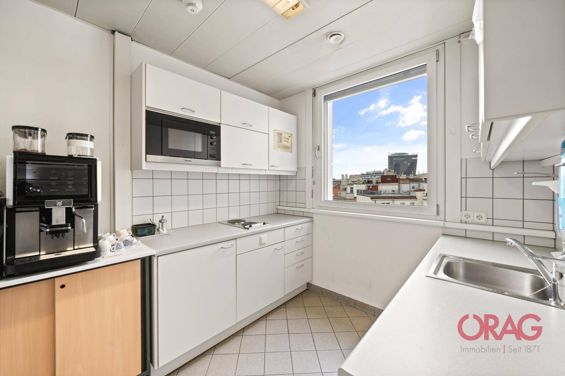 Kleine Küche mit weißen Fliesen, Mikrowelle und Fenster mit Stadtblick.