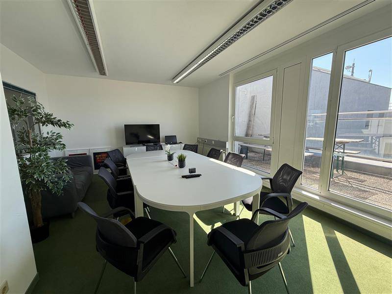 Heller Konferenzraum mit großem ovalen Tisch, bequemen Stühlen und Zugang zu einer sonnigen Dachterrasse.