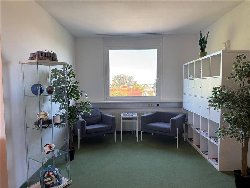 Gemütlicher Wartebereich oder kleines Büro mit zwei Sesseln, einem Fenster und praktischen Regalsystemen.