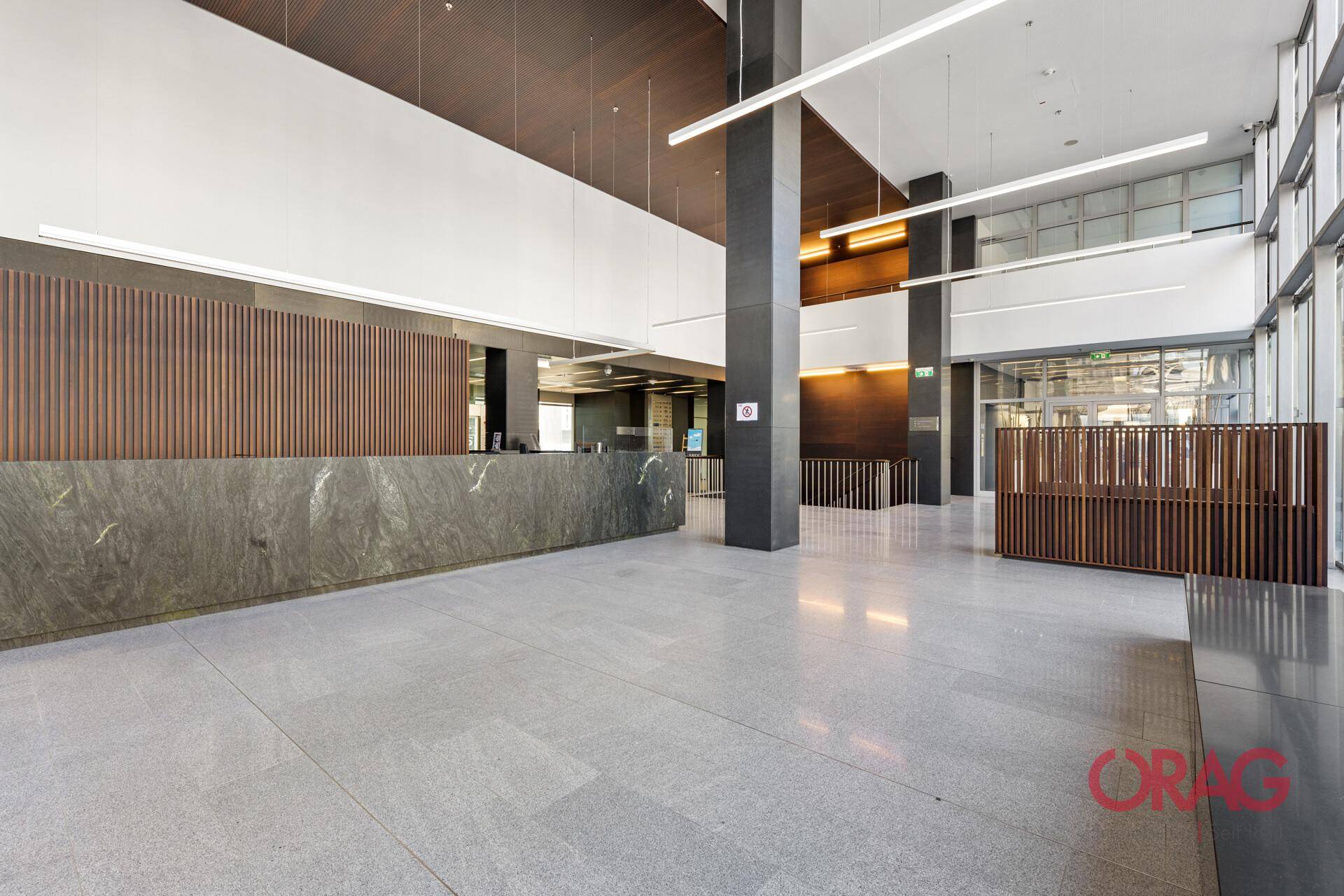 Geräumige, moderne Bürolobby mit langer Rezeptionstheke aus dunklem Stein und hellem Fliesenboden.