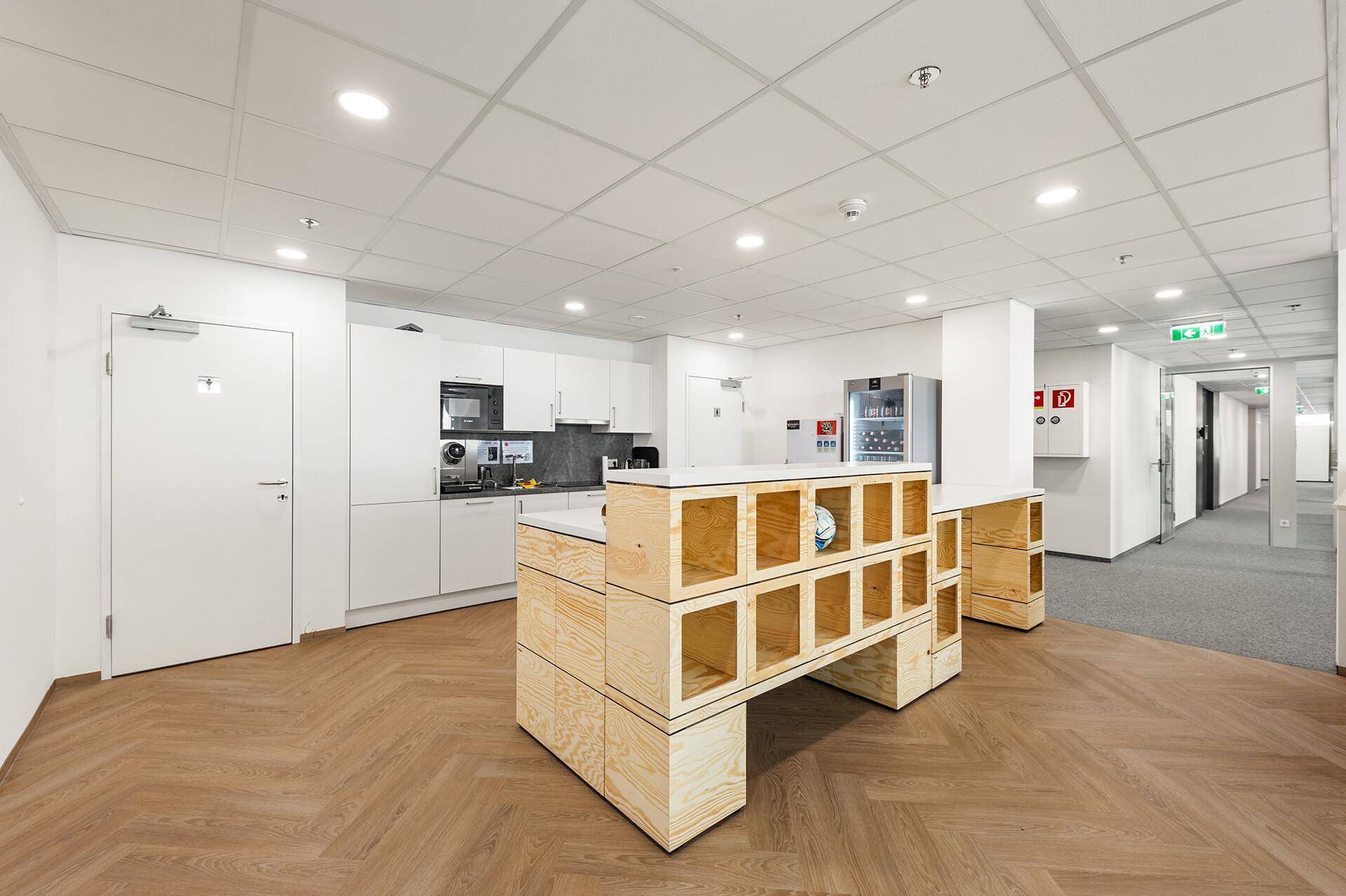 Moderne Büroküche mit weißen Schränken, Holzboden und integrierten Geräten für Mitarbeiter.