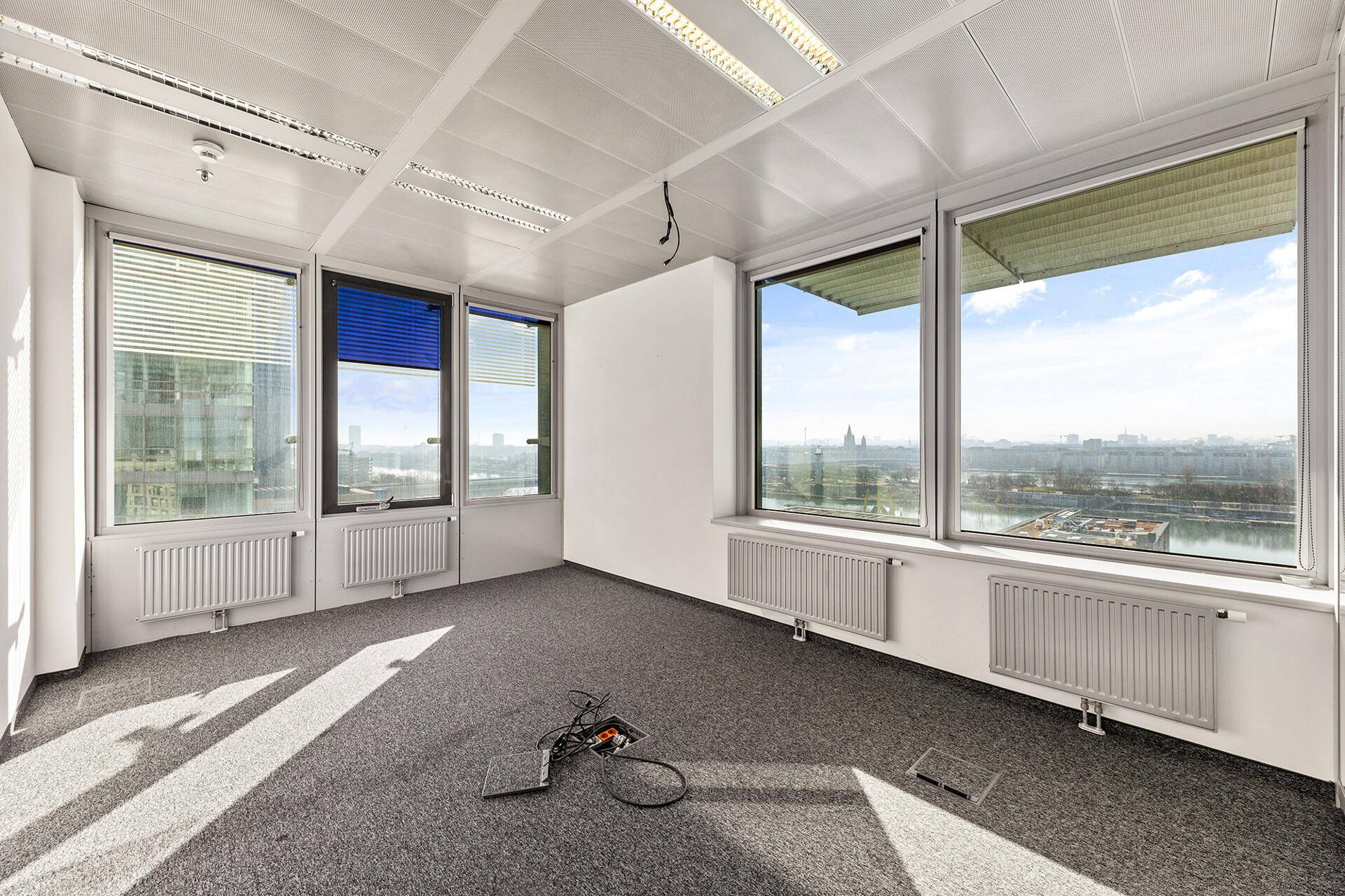 Leeres Büro mit Teppichboden, Rasterdecke und weitem Blick über die Stadt durch große Fenster.