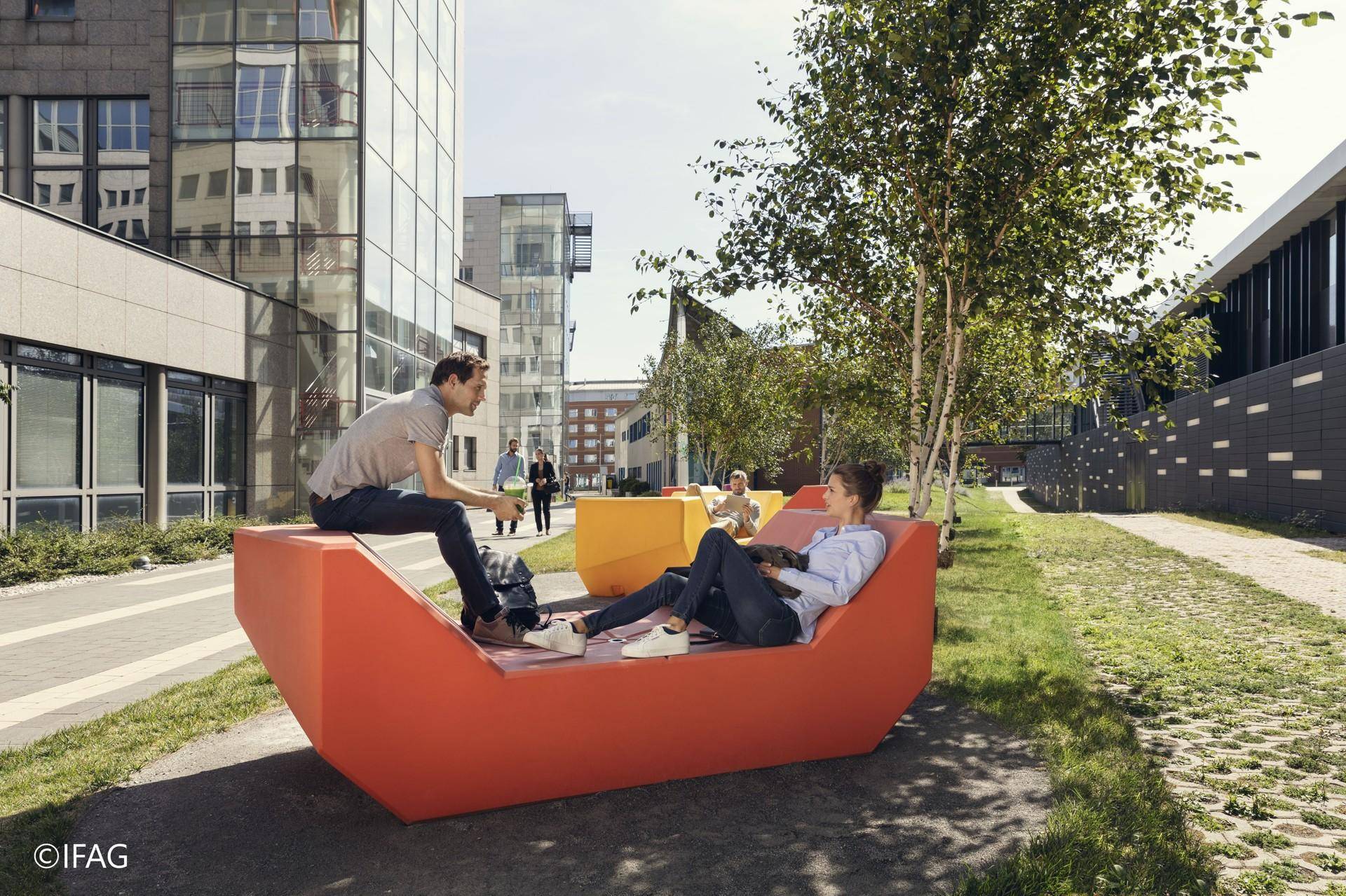 Außenbereich eines modernen Gebäudekomplexes mit Sitzgelegenheiten und Bäumen für Entspannung.