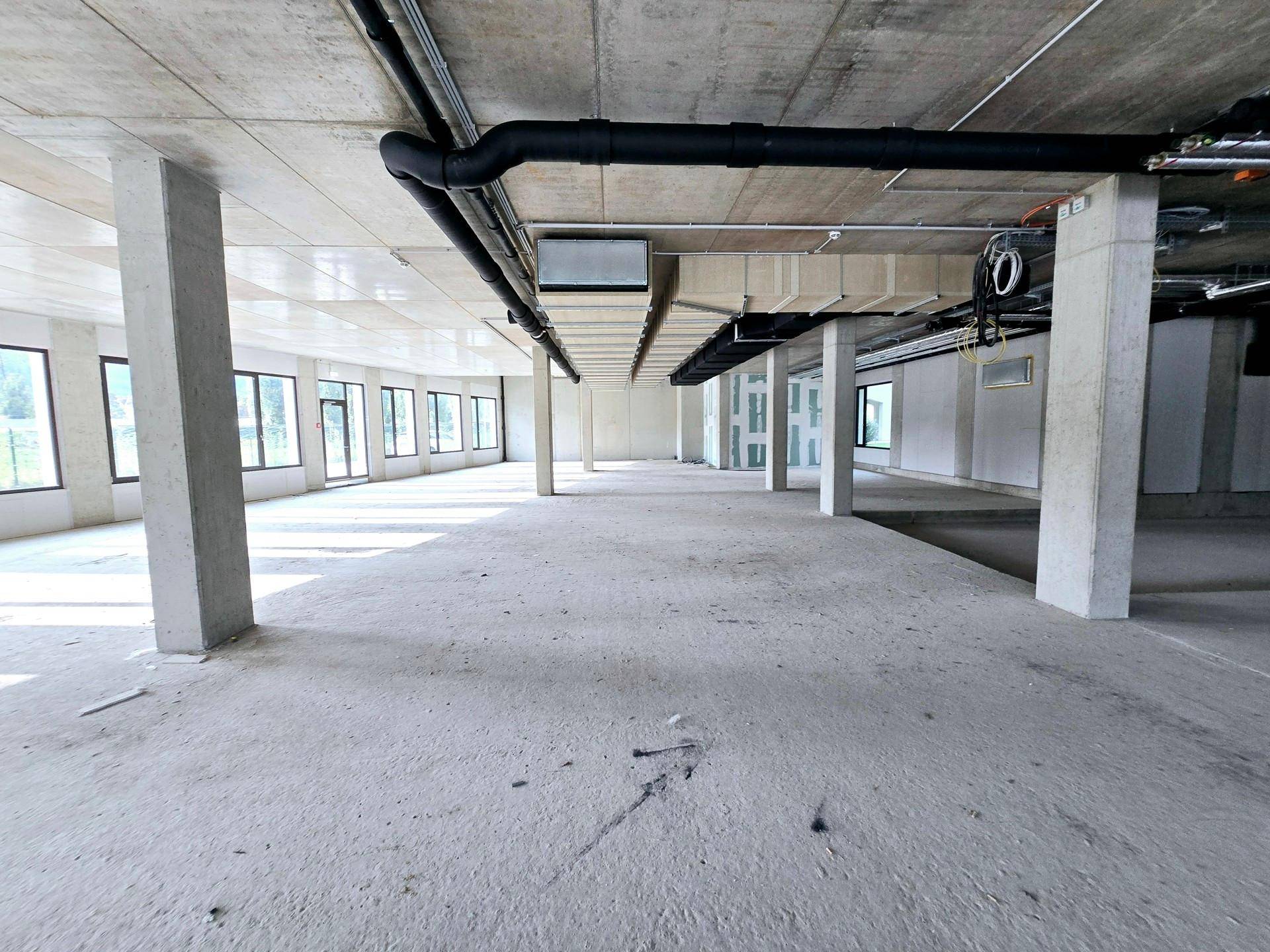Weitläufige Gewerbefläche mit Betonsäulen, freiliegenden Installationen und viel Tageslicht.
