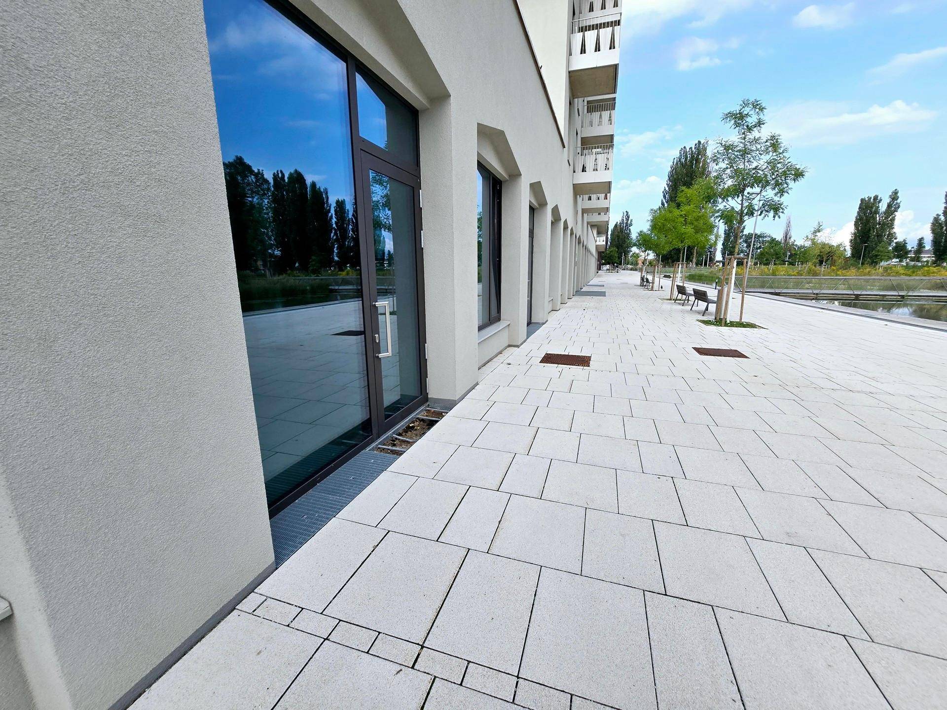 Lange Fassade eines modernen Gebäudes mit großen Fenstern und einem breiten, gefliesten Gehweg.