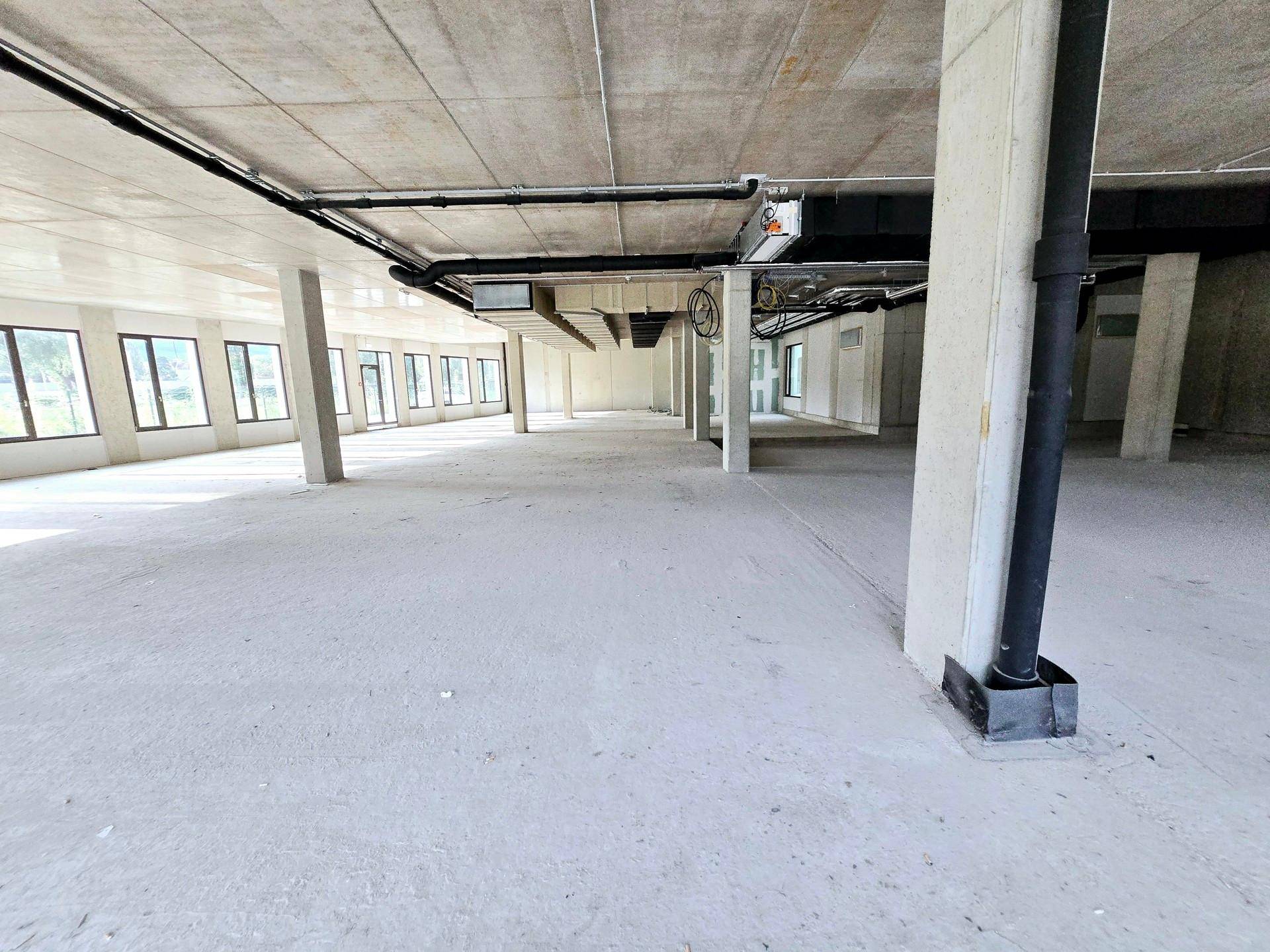 Geräumiger, unfertiger Gewerbebereich mit freiliegenden Leitungen und Betonelementen, bereit für den Ausbau.