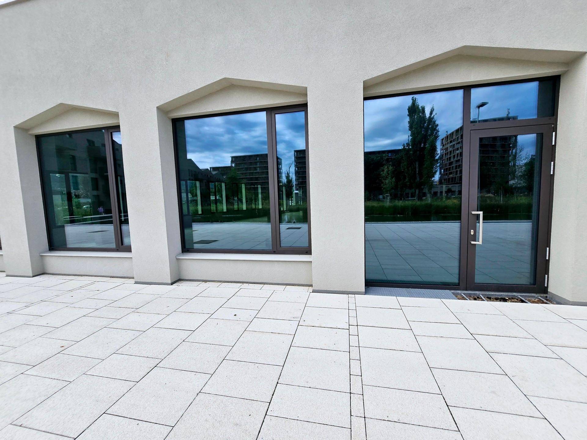 Moderner Geschäftseingang mit großen, reflektierenden Fenstern und hellen Pflastersteinen.