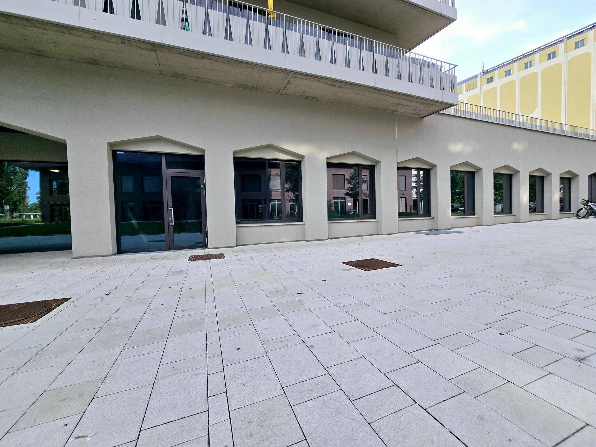 Moderne Gebäudefassade mit ebenerdigen Geschäftsflächen und einem großzügigen gefliesten Außenbereich.