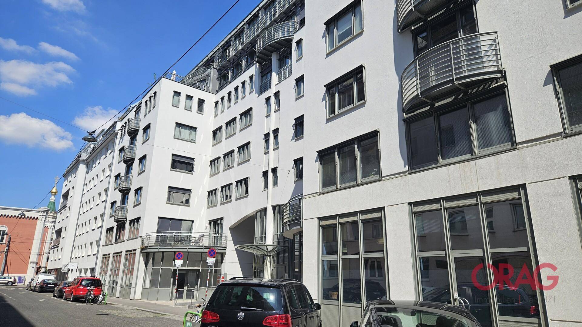 Lange Fassade eines modernen Bürogebäudes mit vielen Fenstern und Balkonen entlang einer städtischen Straße.