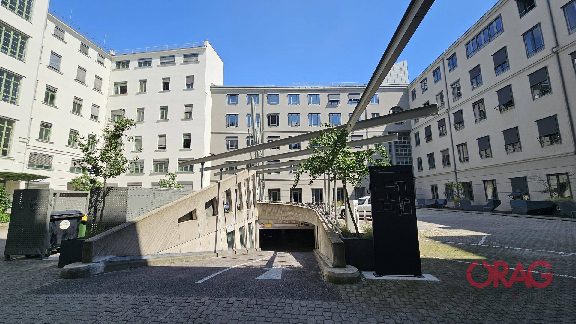 Innenhof mit Zufahrt zu einer Tiefgarage und Fahrradständern, umgeben von modernen Gebäuden.
