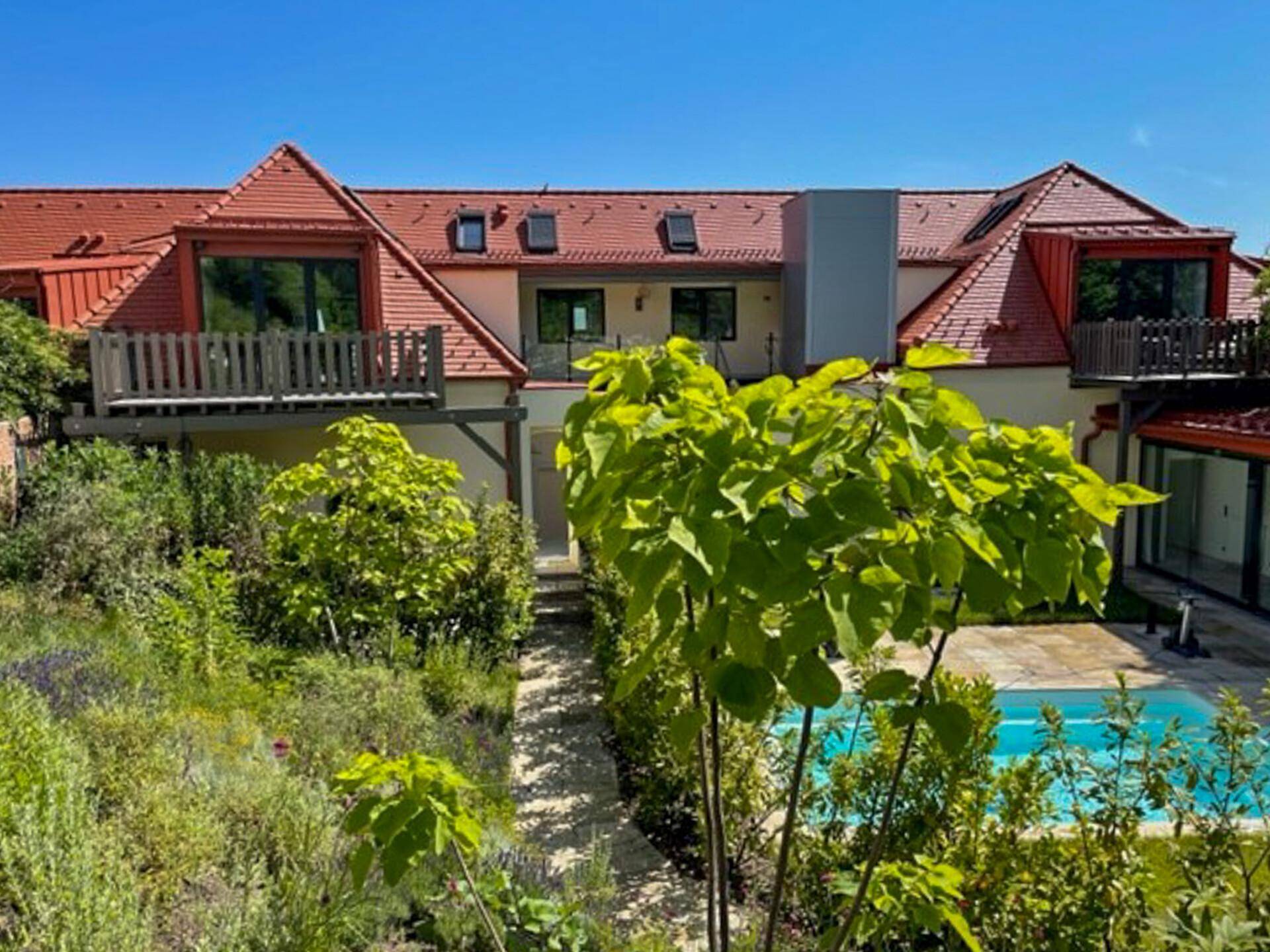 Rückansicht des Gebäudes mit mehreren Balkonen und einem gepflegten Gartenbereich mit Swimmingpool.
