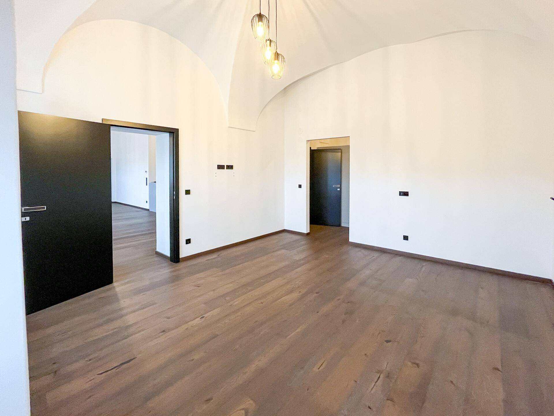 Geräumiger, heller Raum mit hohen Gewölbedecken, dunklem Holzfußboden und schwarzen Türen.