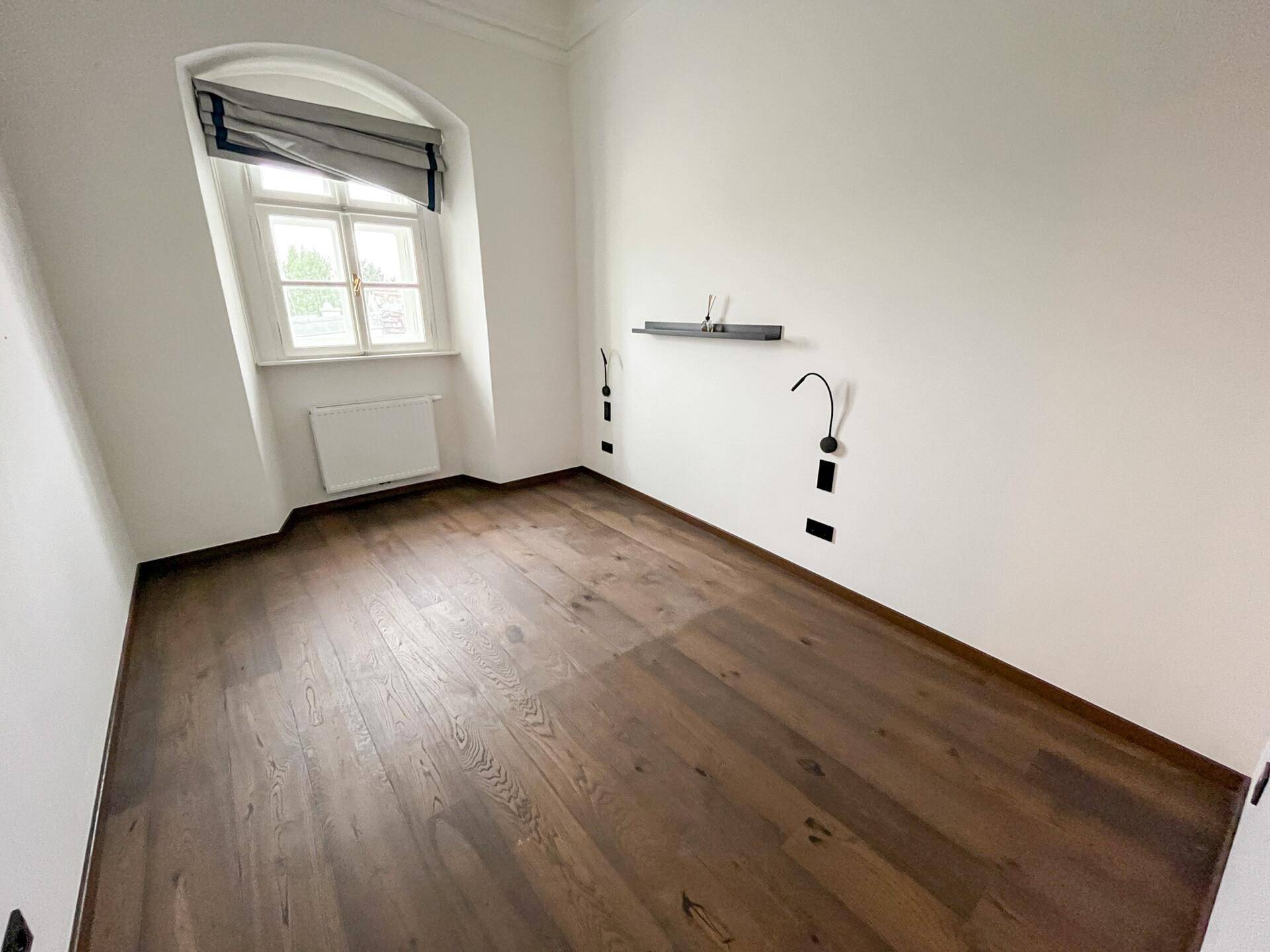 Helles Schlafzimmer mit dunklem Holzfußboden, Gewölbedecke und einem Fenster mit Blick nach draußen.