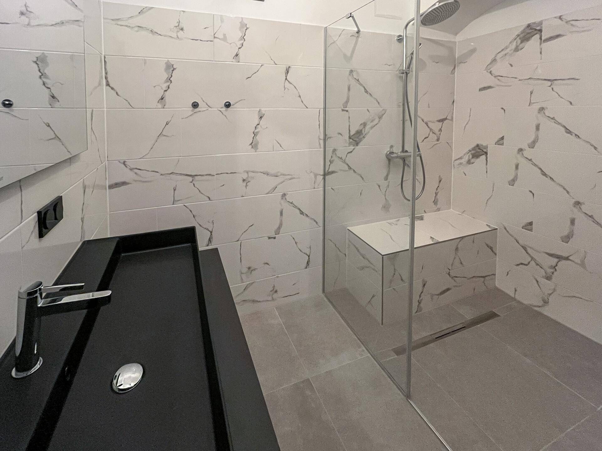 Modernes Badezimmer mit großformatigen Marmorfliesen, ebenerdiger Dusche und schwarzem Waschtisch.