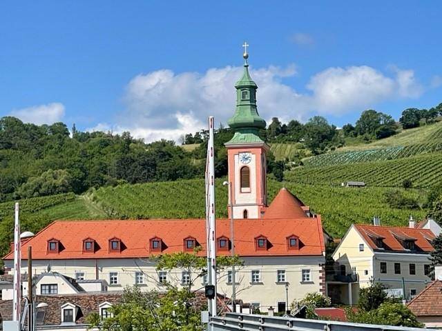 Malerischer Blick auf eine Kirche mit grüner Kuppel, umgeben von Weinbergen und Hügeln.
