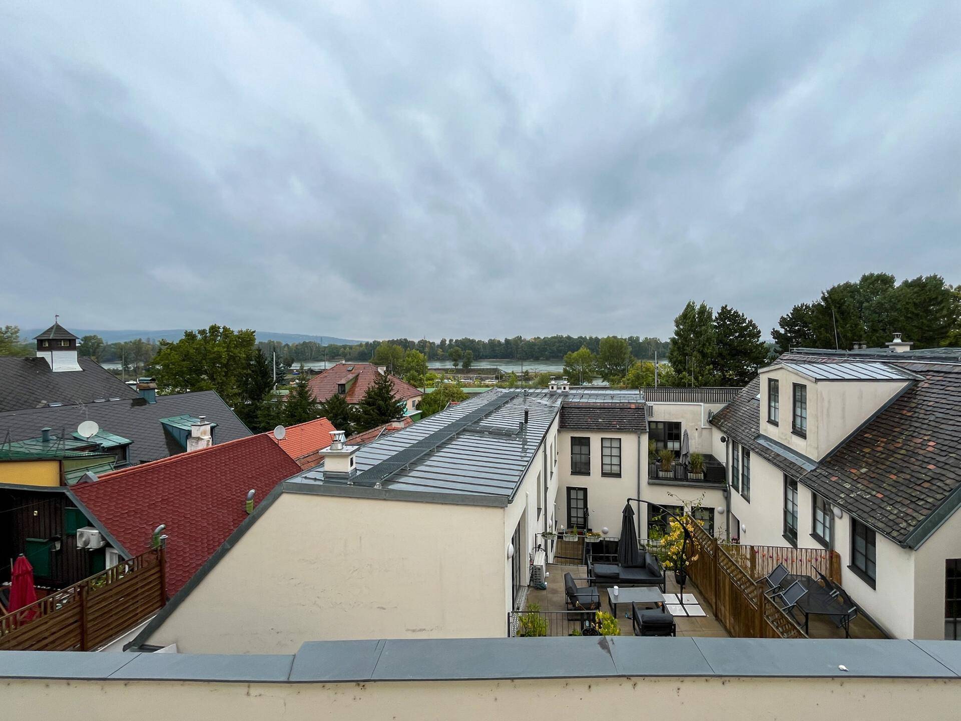 Weitläufiger Blick über Dächer, einen Innenhof und den See im Hintergrund unter bewölktem Himmel.