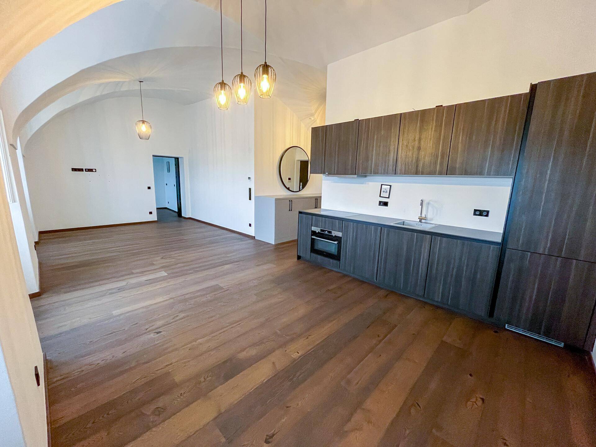 Offener Wohnbereich mit moderner Einbauküche, dunklen Holzfronten und eleganten Pendelleuchten.
