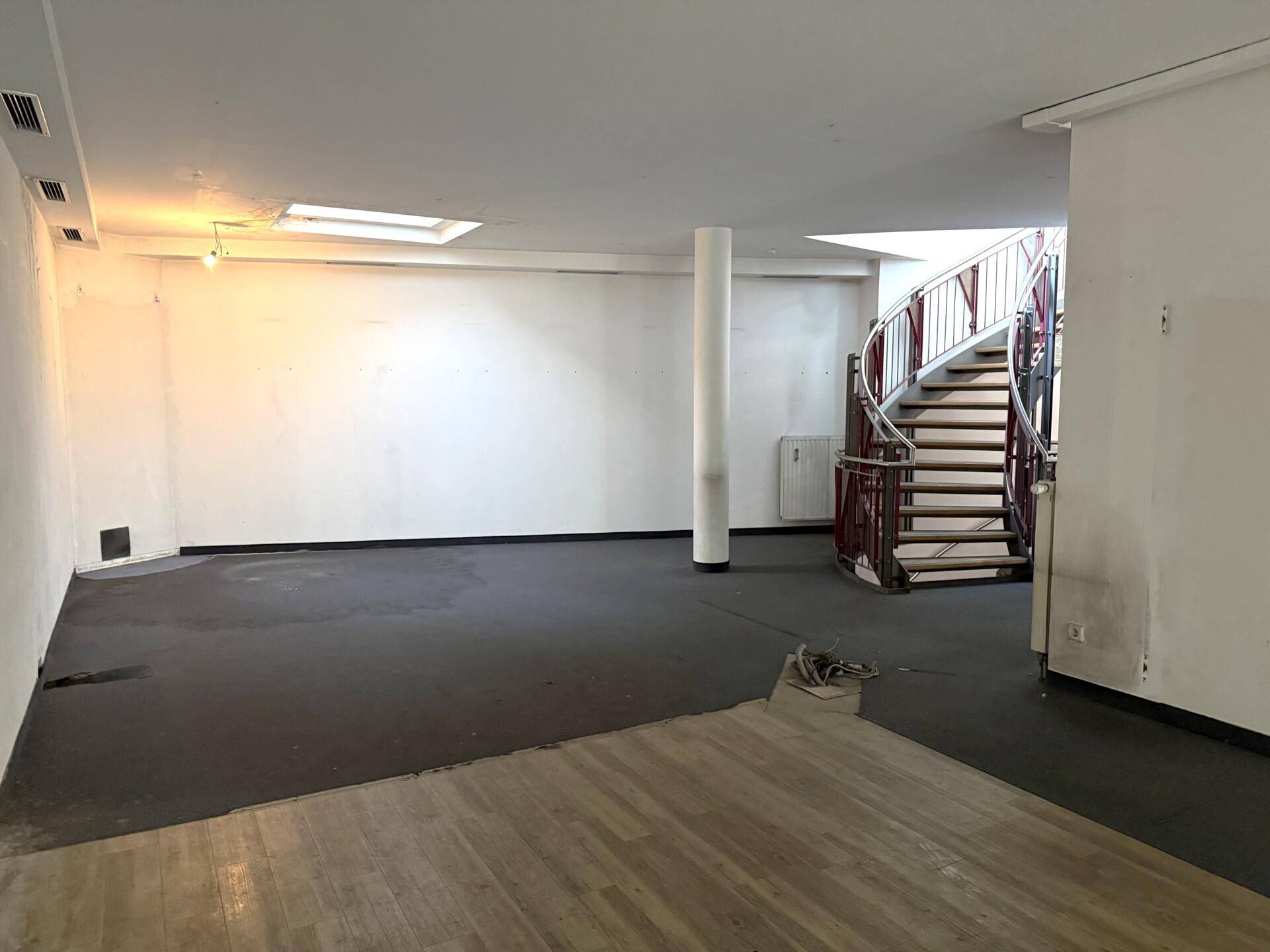 Großer offener Gewerberaum mit einer eleganten Wendeltreppe, gemischtem Bodenbelag und einem Oberlicht für natürliches Licht.