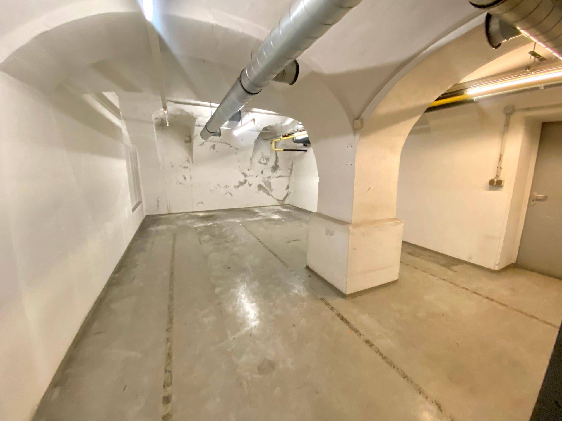 Geräumiger Kellerraum mit charakteristischen Gewölbedecken, Betonboden und sichtbaren Versorgungsleitungen, ideal als Lagerfläche.