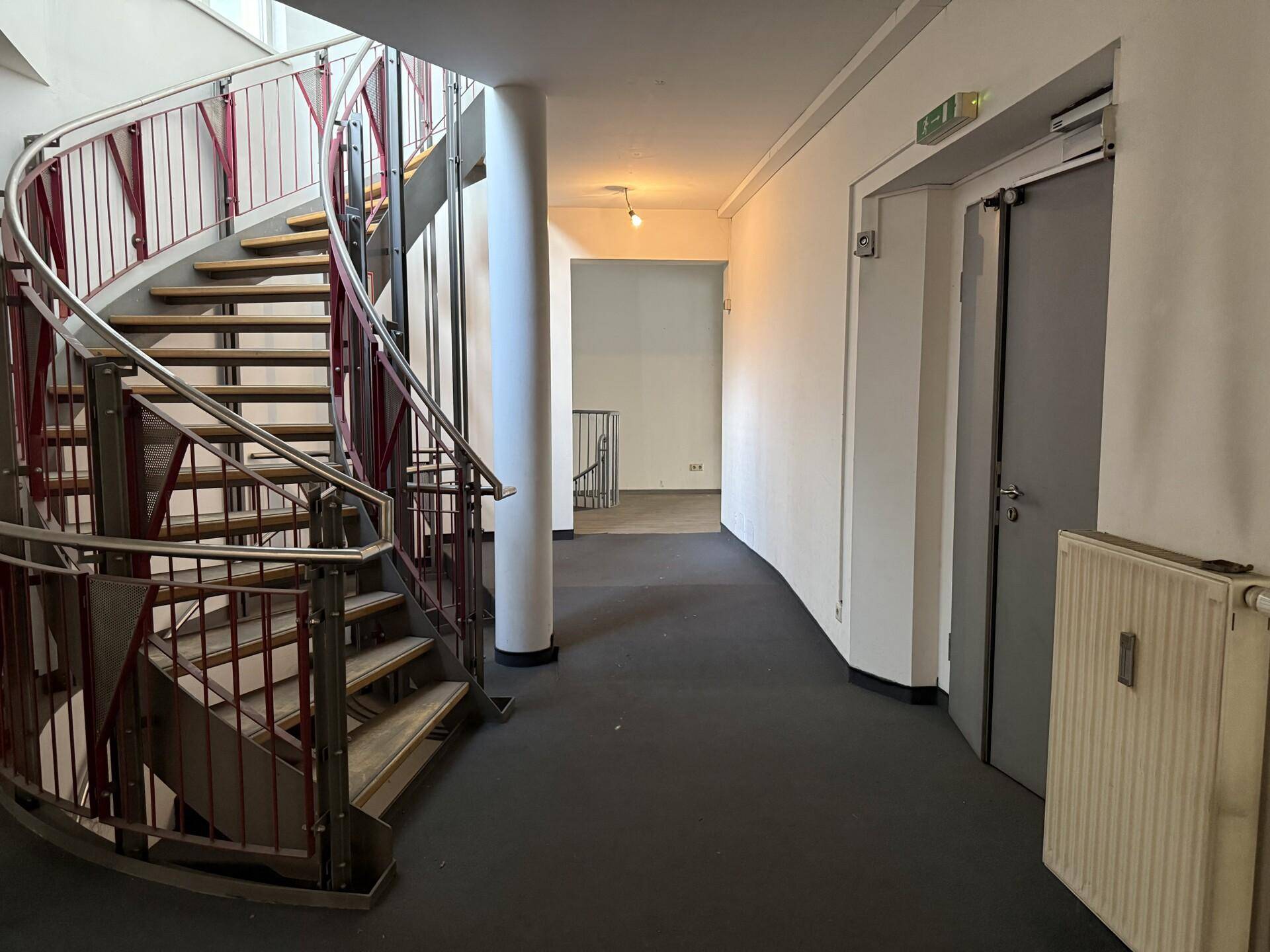 Geräumiger Flur mit einer markanten Wendeltreppe, einer Tür und einem Heizkörper an der Wand, gut beleuchtet.