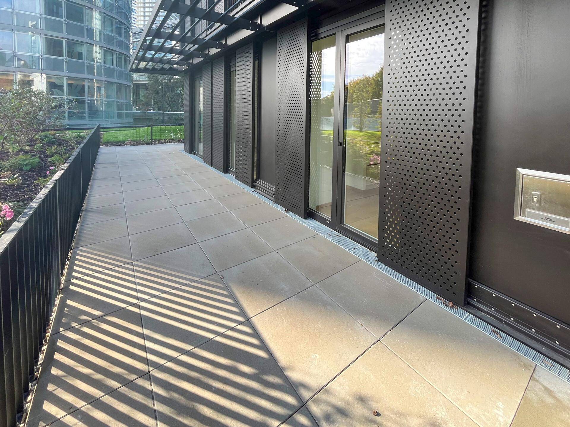 Gepflasterte Außenterrasse mit modernen, perforierten Paneelen und großen Glasfronten.