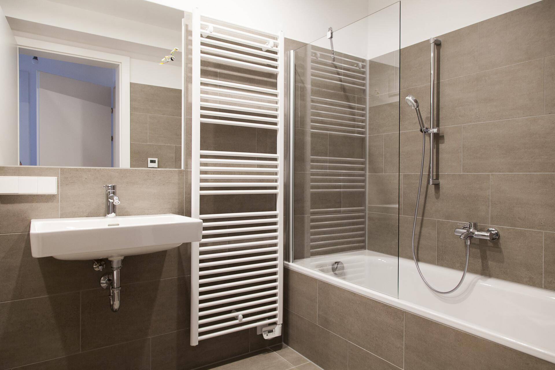 Modernes Badezimmer mit braunen Fliesen, Badewanne und beheiztem Handtuchhalter.