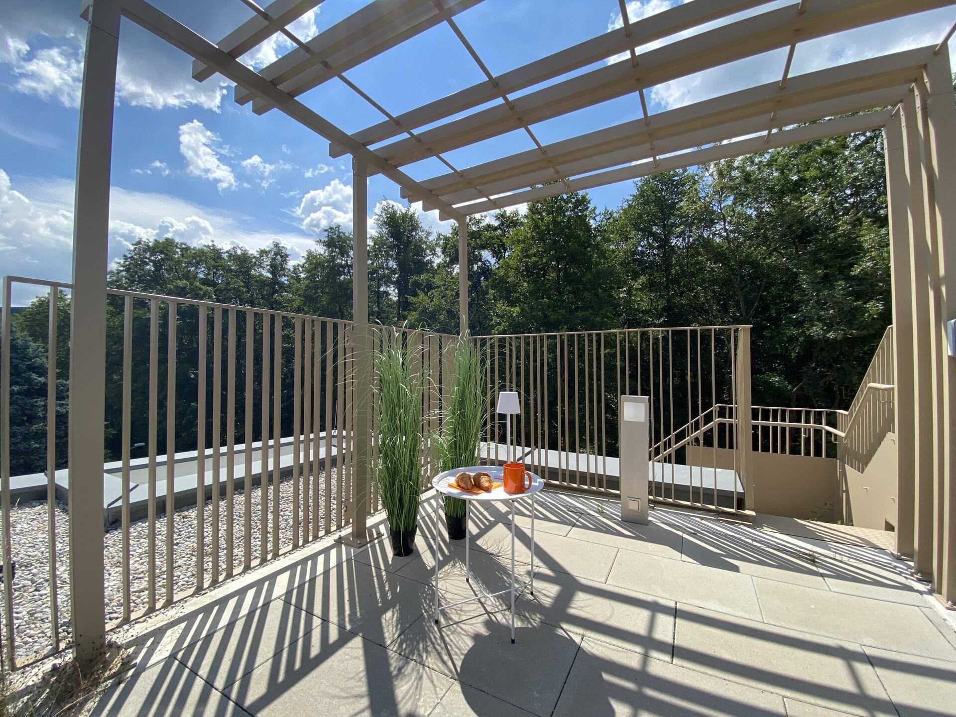 Sonnige Dachterrasse mit Pergola, gemütlicher Sitzecke und Blick ins Grüne.