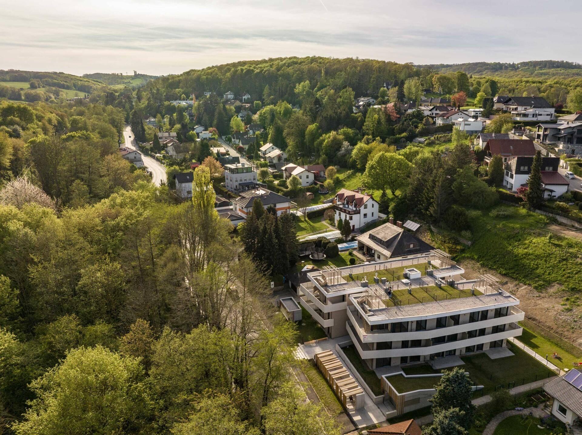 Luftaufnahme der modernen Wohnanlage eingebettet in eine grüne, hügelige Landschaft.