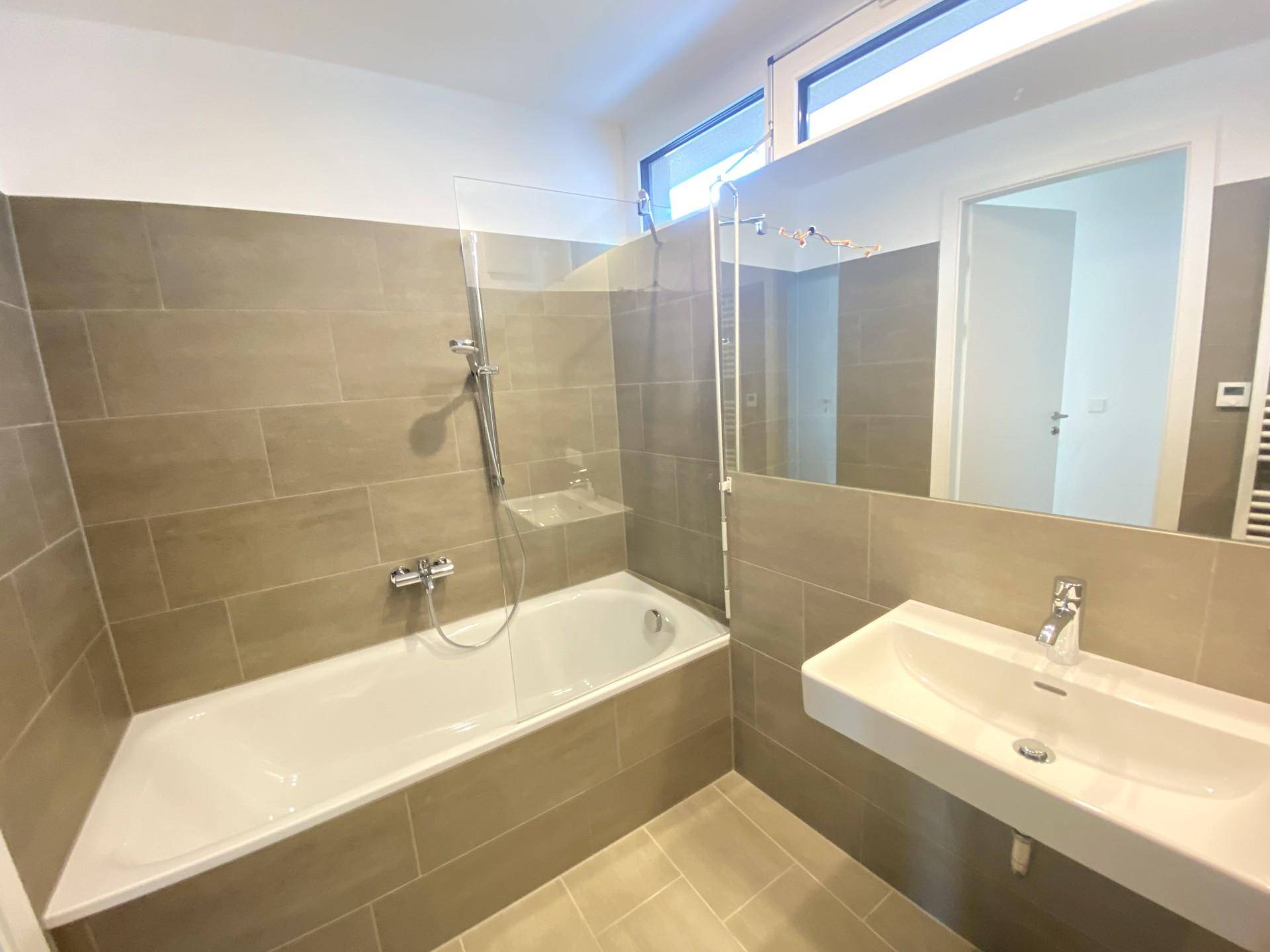 Modernes Badezimmer mit Badewanne, Waschbecken und hellen, großformatigen Fliesen.