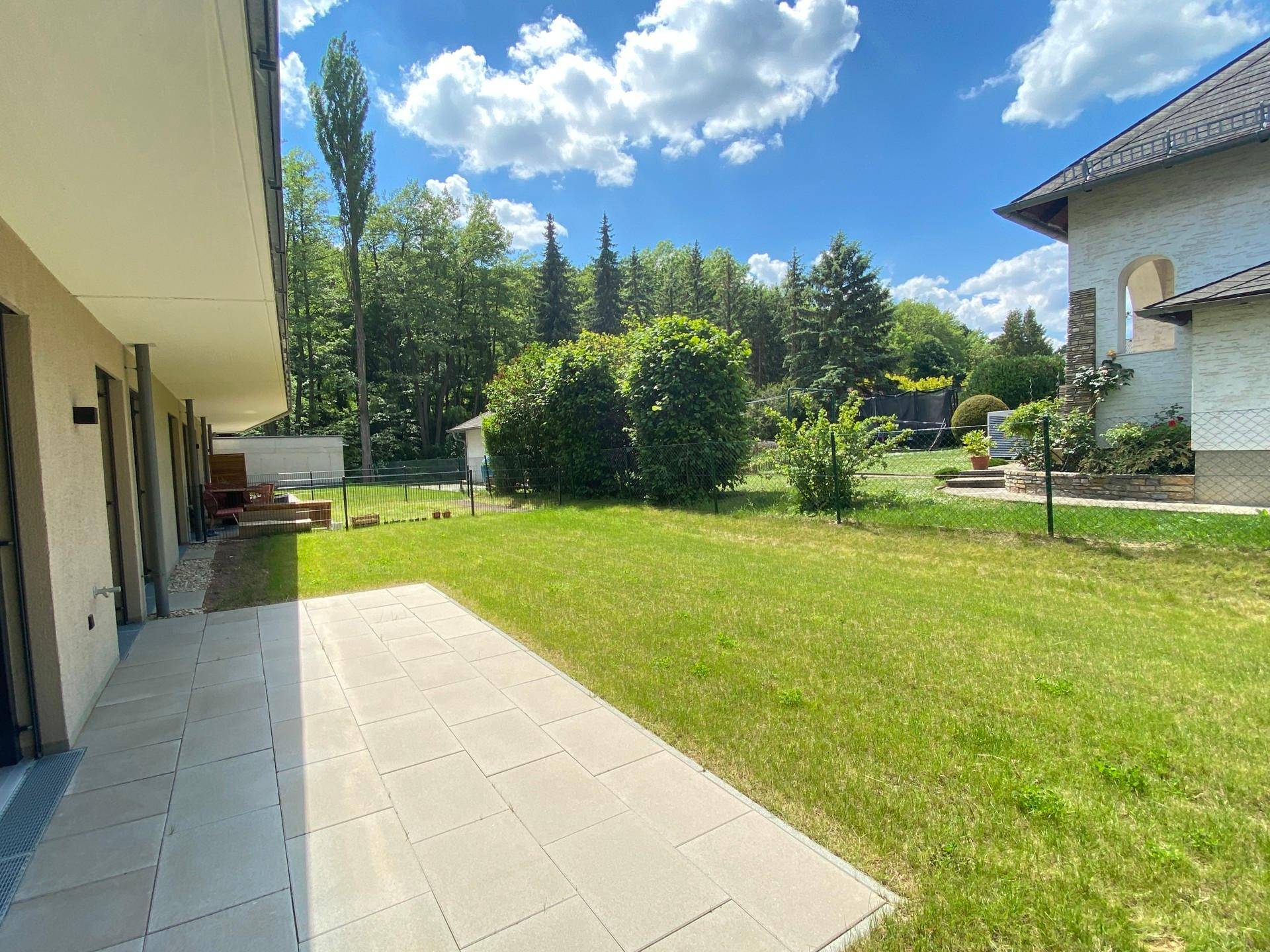 Geräumige, gepflasterte Terrasse grenzt an einen großen Gartenbereich mit Bäumen und Büschen.