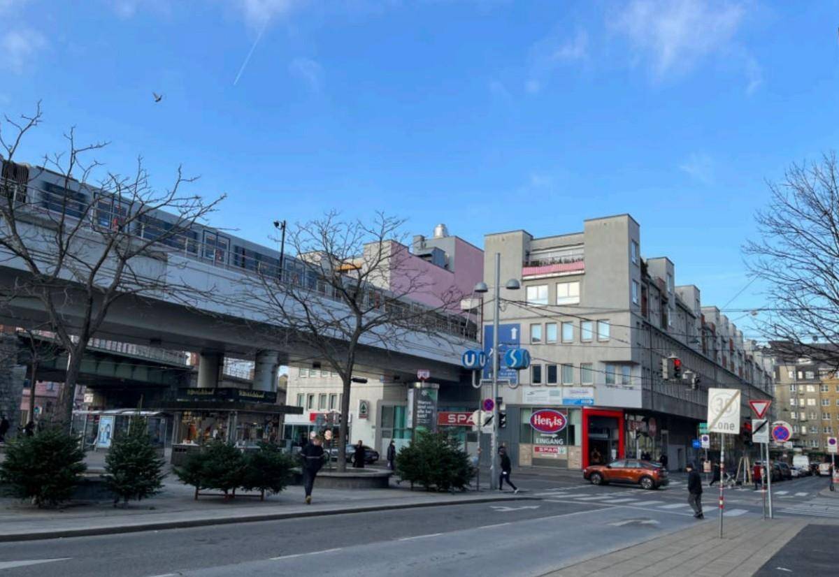 Weitwinkelansicht einer städtischen Straße mit Geschäften, Gebäuden und einer erhöhten U-Bahn-Linie.