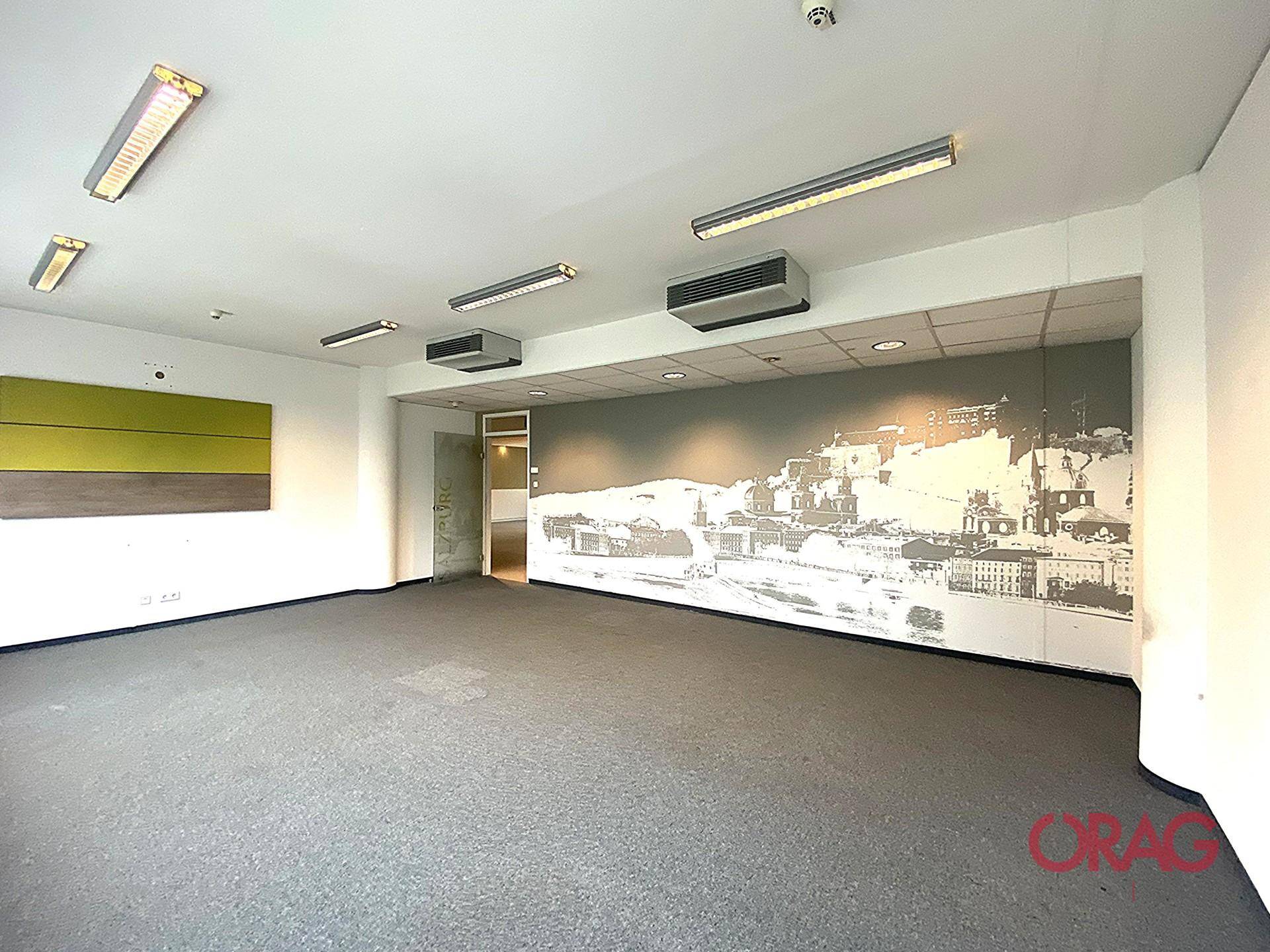 Großer Büroraum mit Teppichboden und verschiedenen Wanddekorationen, bereit zur sofortigen Nutzung.