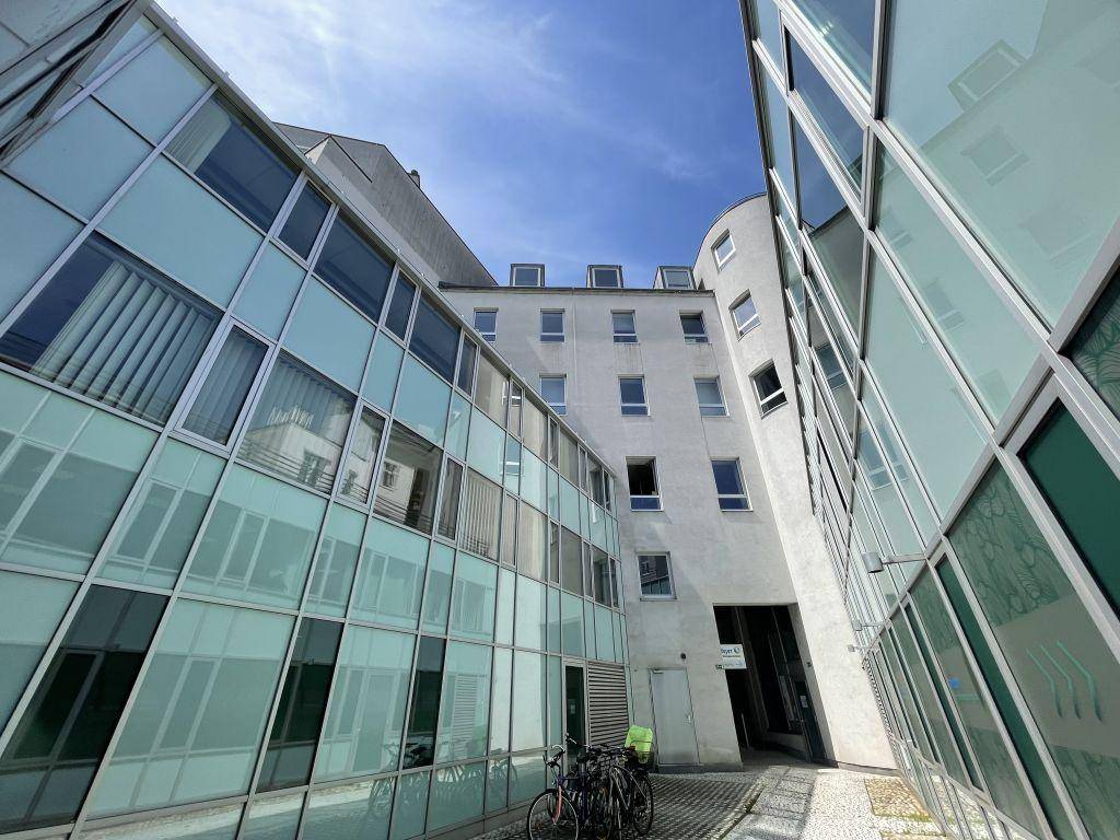 Blick auf die moderne Glasfassade eines Gebäudes im Innenhof mit abgestellten Fahrrädern.