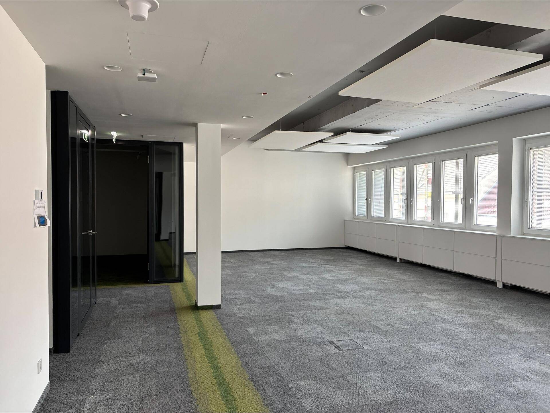 Großer, leerer Büroraum mit Teppichboden, Glaswänden und vielen Fenstern für eine helle Arbeitsumgebung.