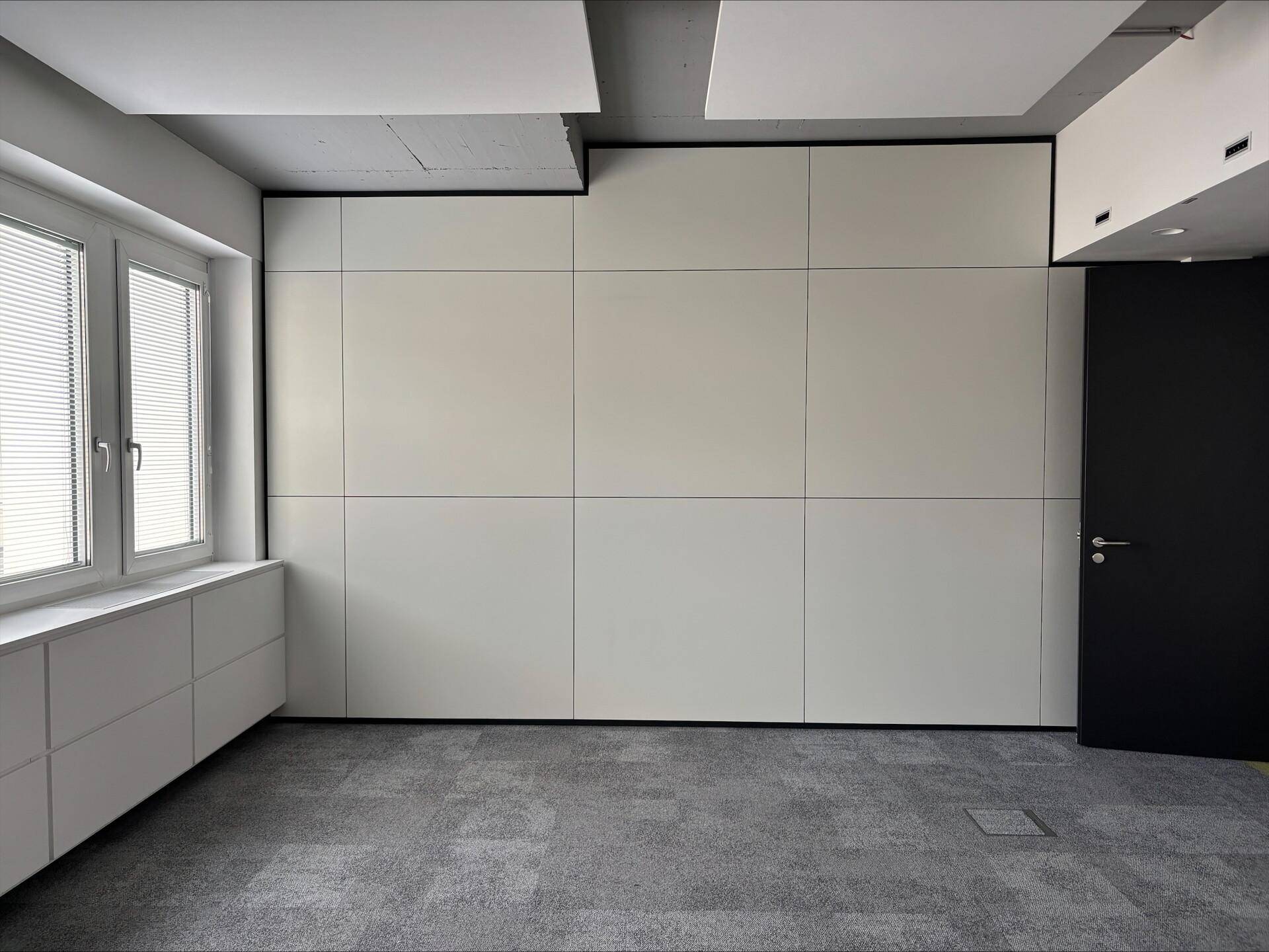 Leerer Büroraum mit Teppichboden, einer großen weißen Wand und einer schwarzen Tür, bereit zur Gestaltung.