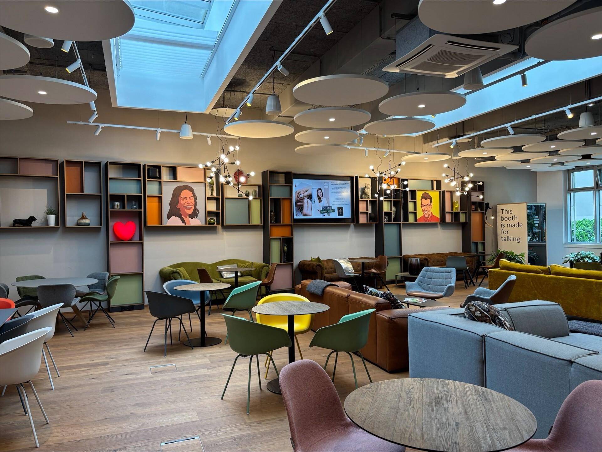 Geräumiger Lounge-Bereich mit vielfältigen Sitzgelegenheiten, modernen Bildschirmen und Oberlichtern, die für Helligkeit sorgen.
